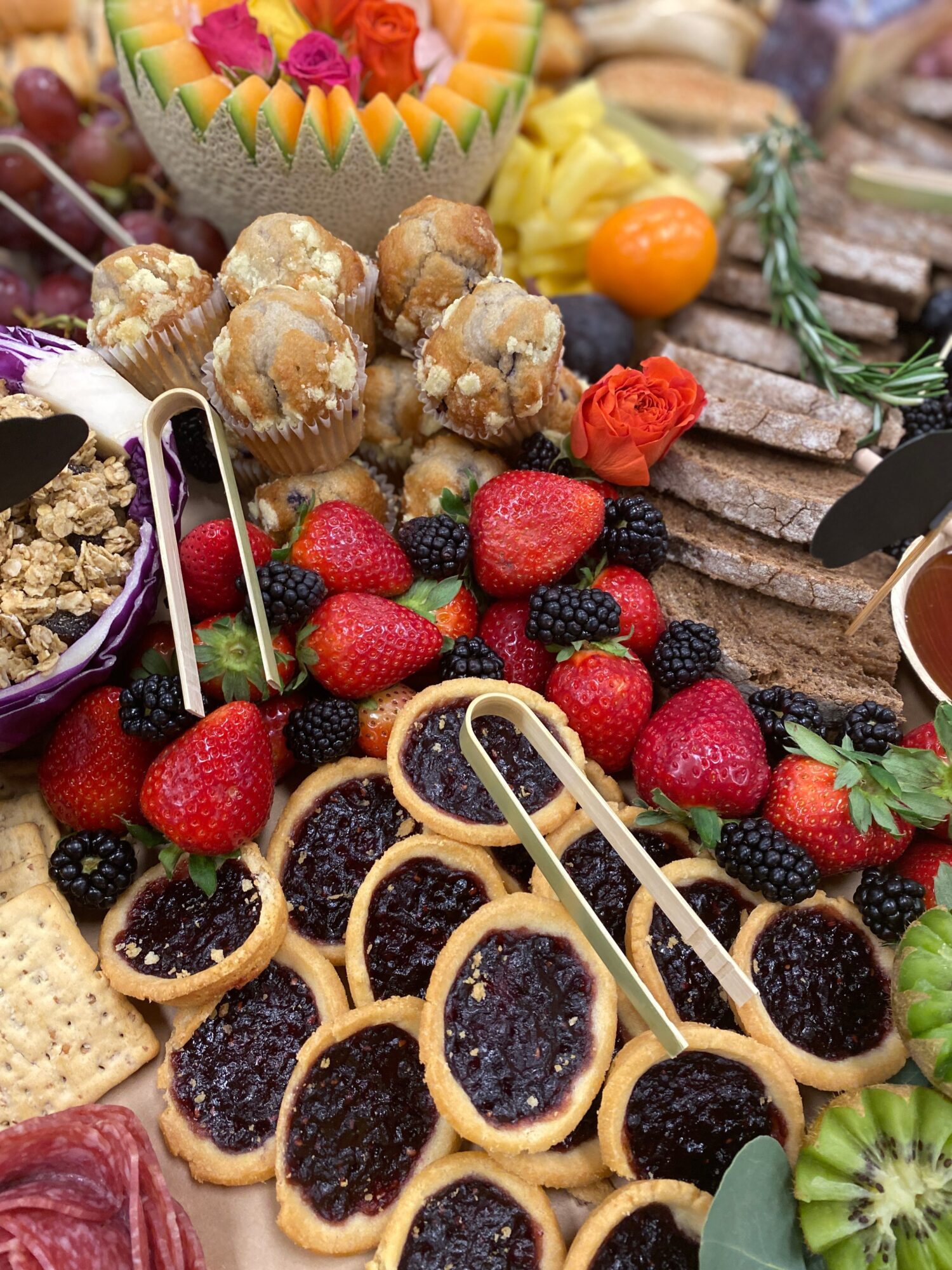 Assorted desserts including strawberries, cookies with jam, and a fruit tart with colorful toppings, arranged on a table.