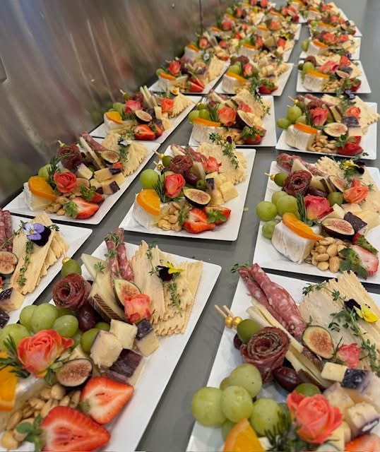Assorted fruit and cheese appetizers on white plates, arranged on a table, with strawberries, grapes, and sliced fruits, garnished with herbs and flowers.