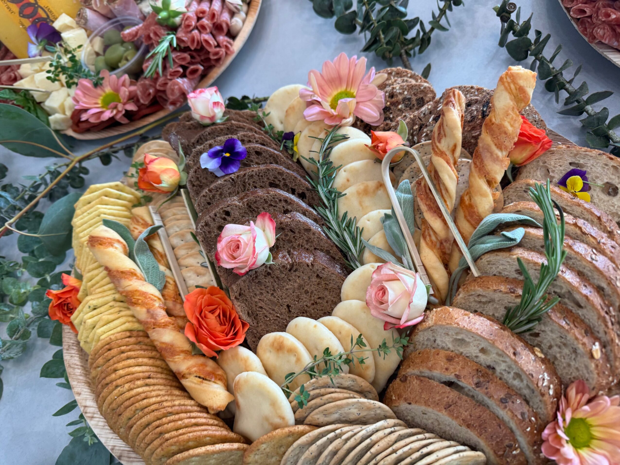 Assorted sliced cakes and bread arranged on a table with flowers and greenery, including chocolate, vanilla, and fruit-flavored slices.