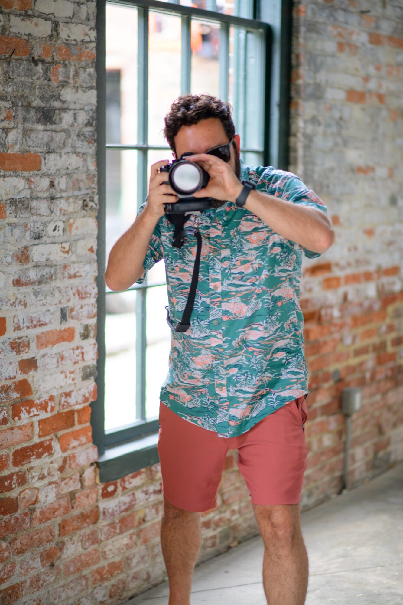 Person taking a photo with a camera, standing near a window in a brick-walled room.