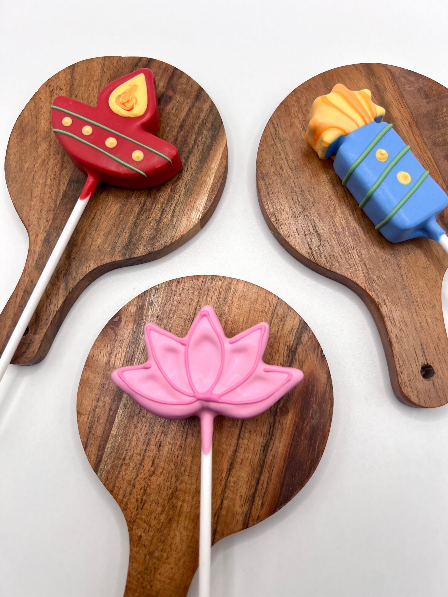 Three decorated cookies on wooden paddles: a red fish, a blue fish, and a pink lotus flower, on a white surface.