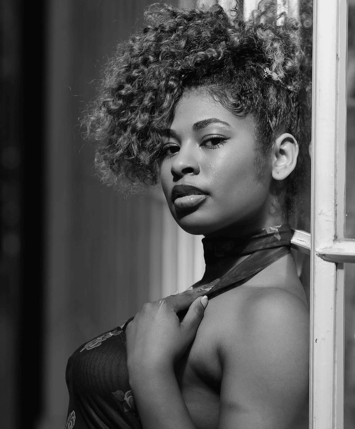 Portrait of a woman with curly hair, looking at the camera, holding a scarf near her neck, in black and white.