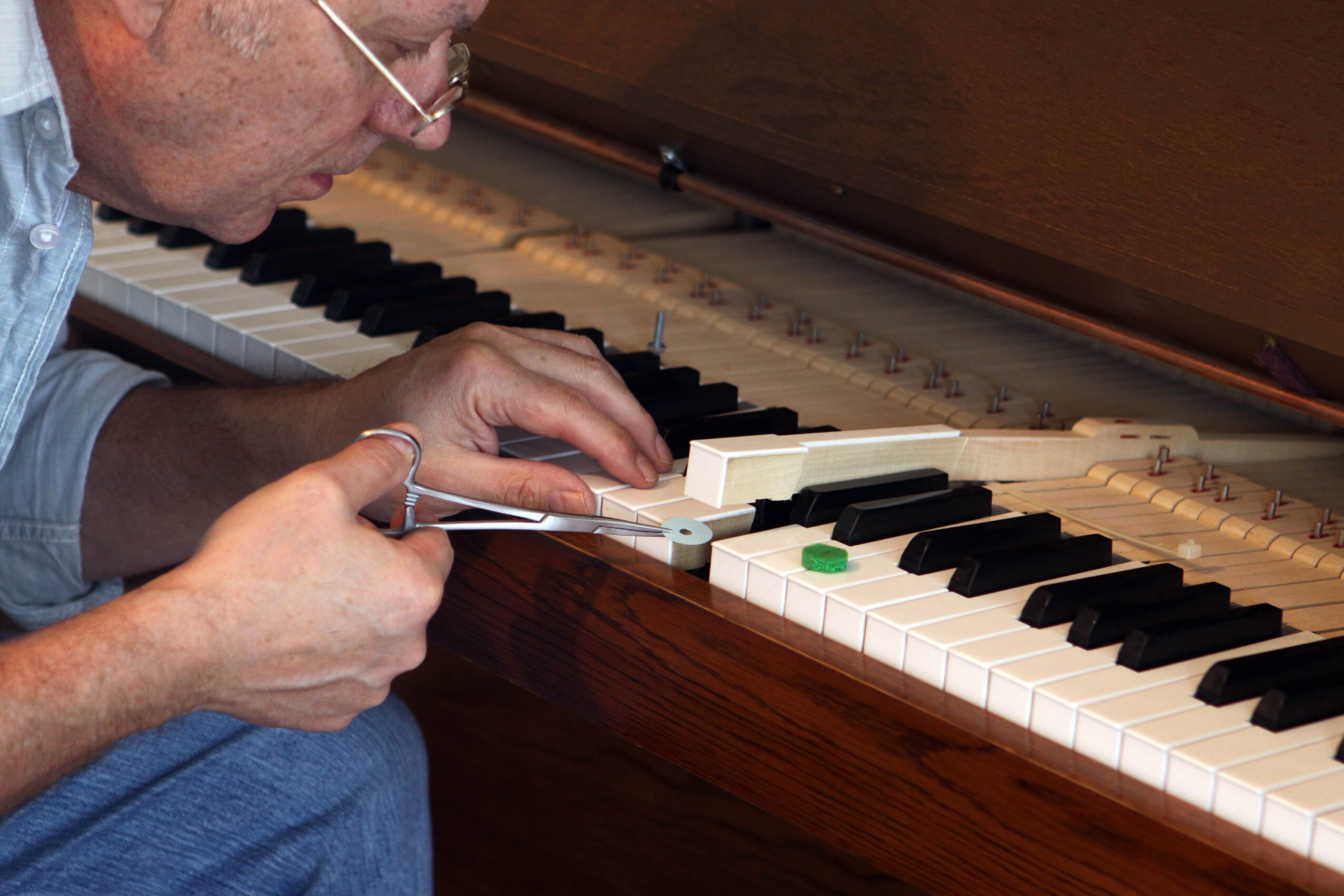 Person adjusting a tuning device on a piano keyboard, focusing on the keys and tuning process.