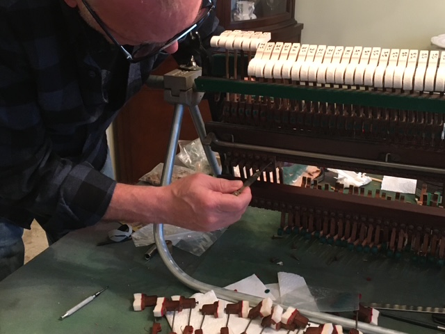 Person working on a mechanical device with rows of small components, using a tool on a green work surface.