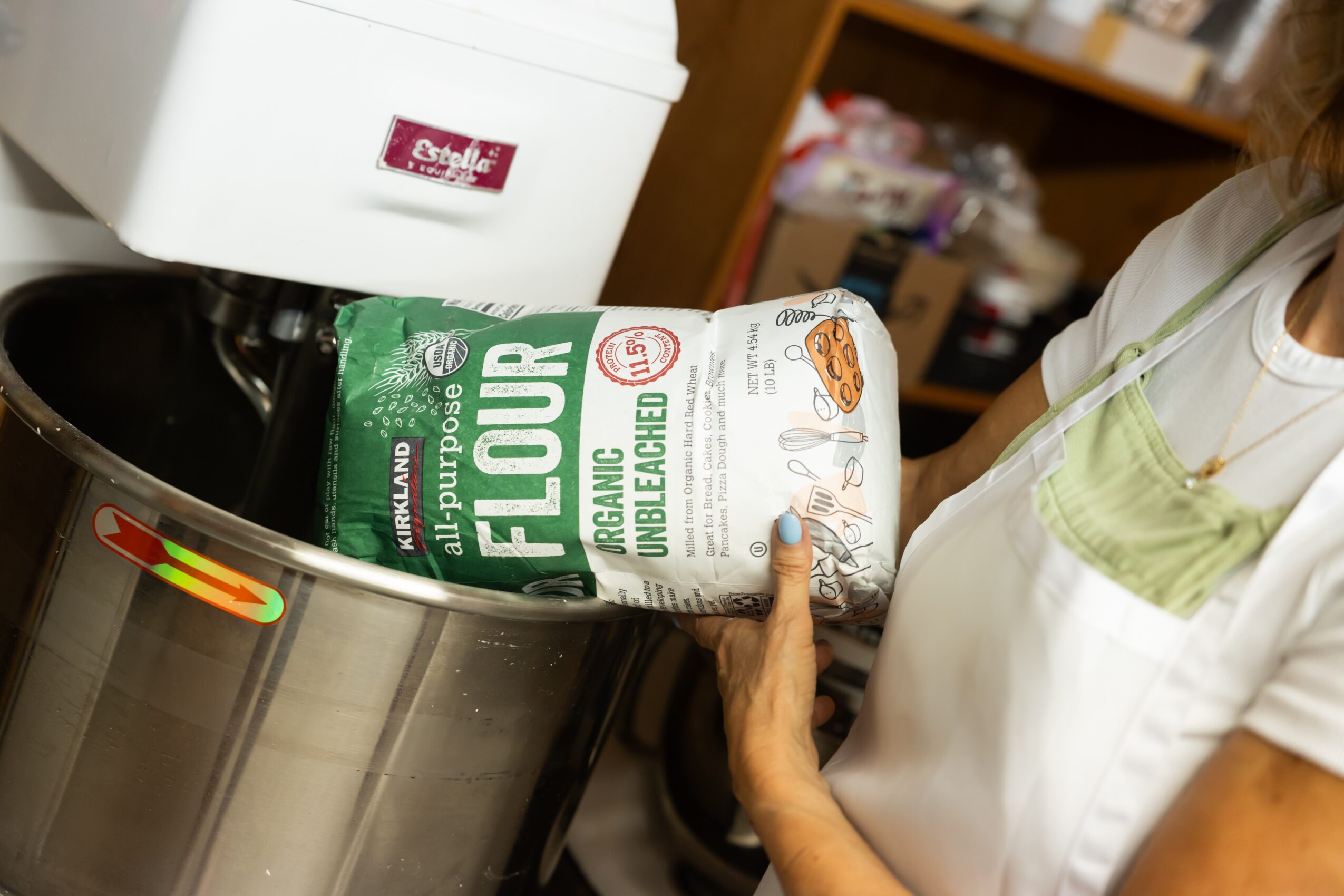 Person holding a bag of organic whole wheat flour near a kitchen appliance, with a shelf in the background.