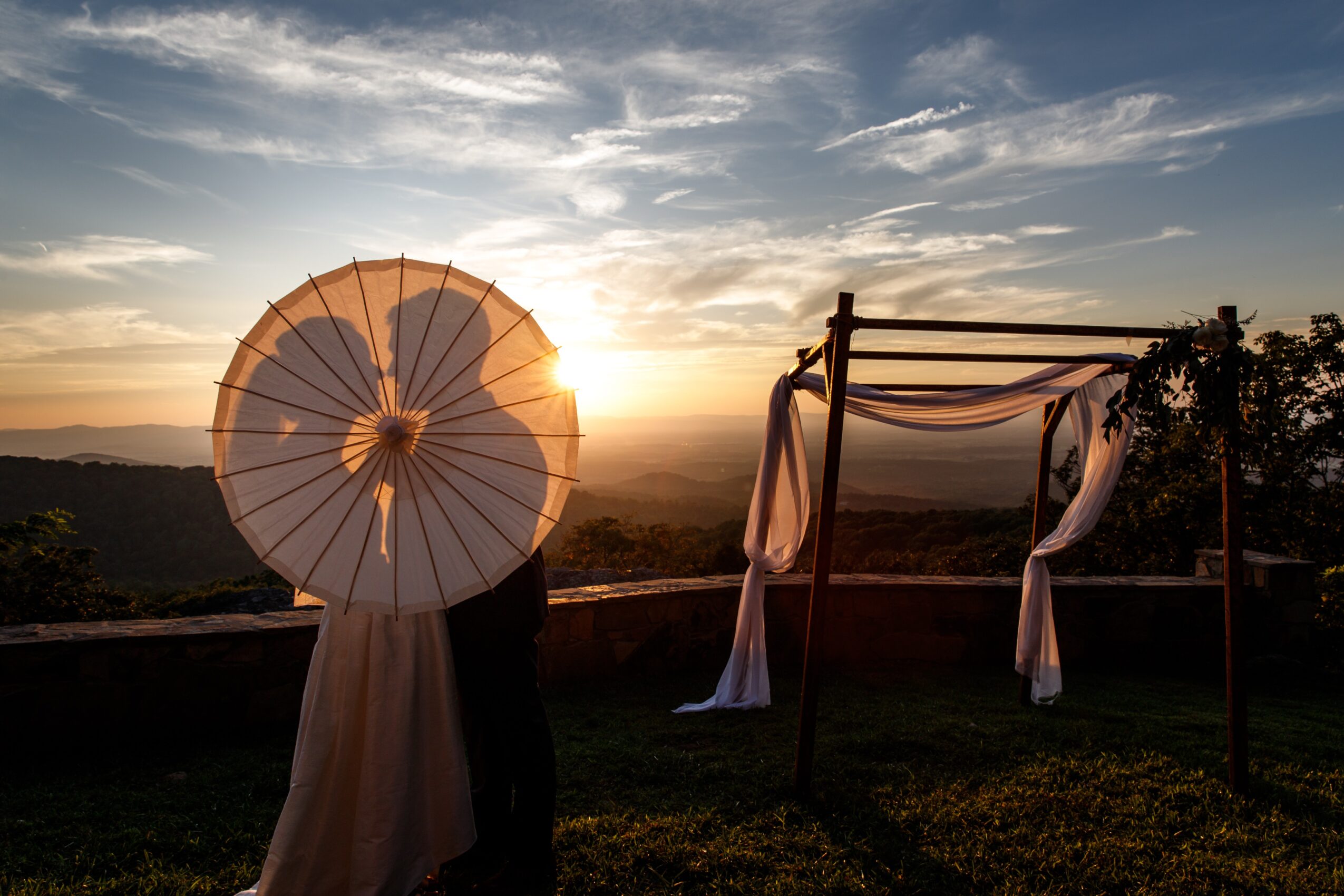 Sunset over landscape with umbrella and outdoor canopy, sky with clouds, and distant hills.