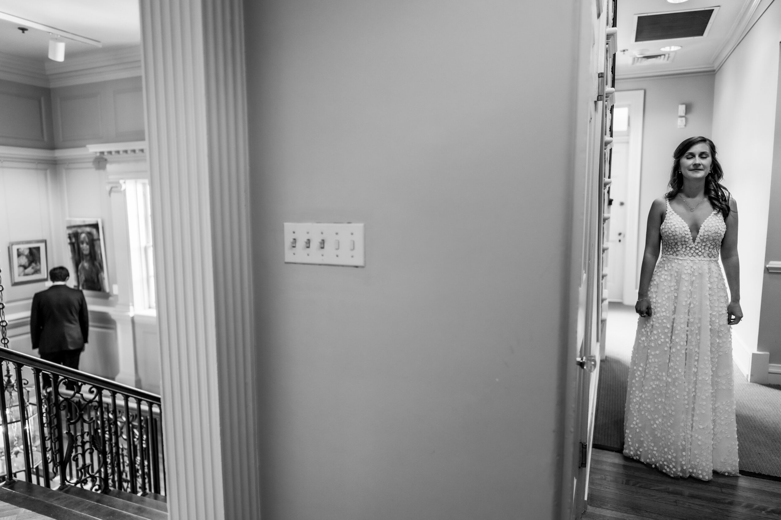 Gallery with people viewing artwork, woman in a long dress standing in a hallway, black and white photo.