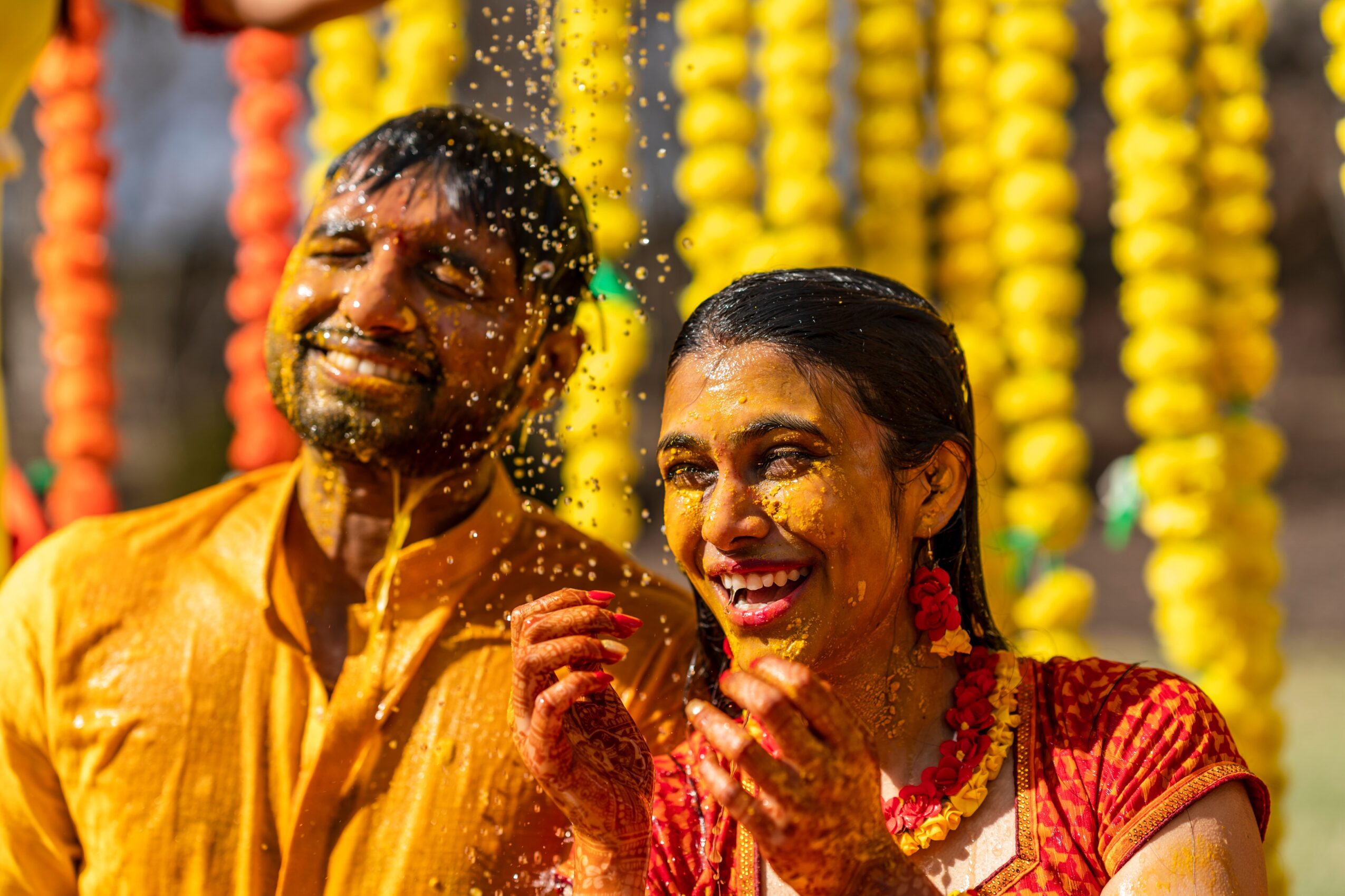 A man and woman celebrating with water splashing, colorful decorations in the background, smiling and joyful.