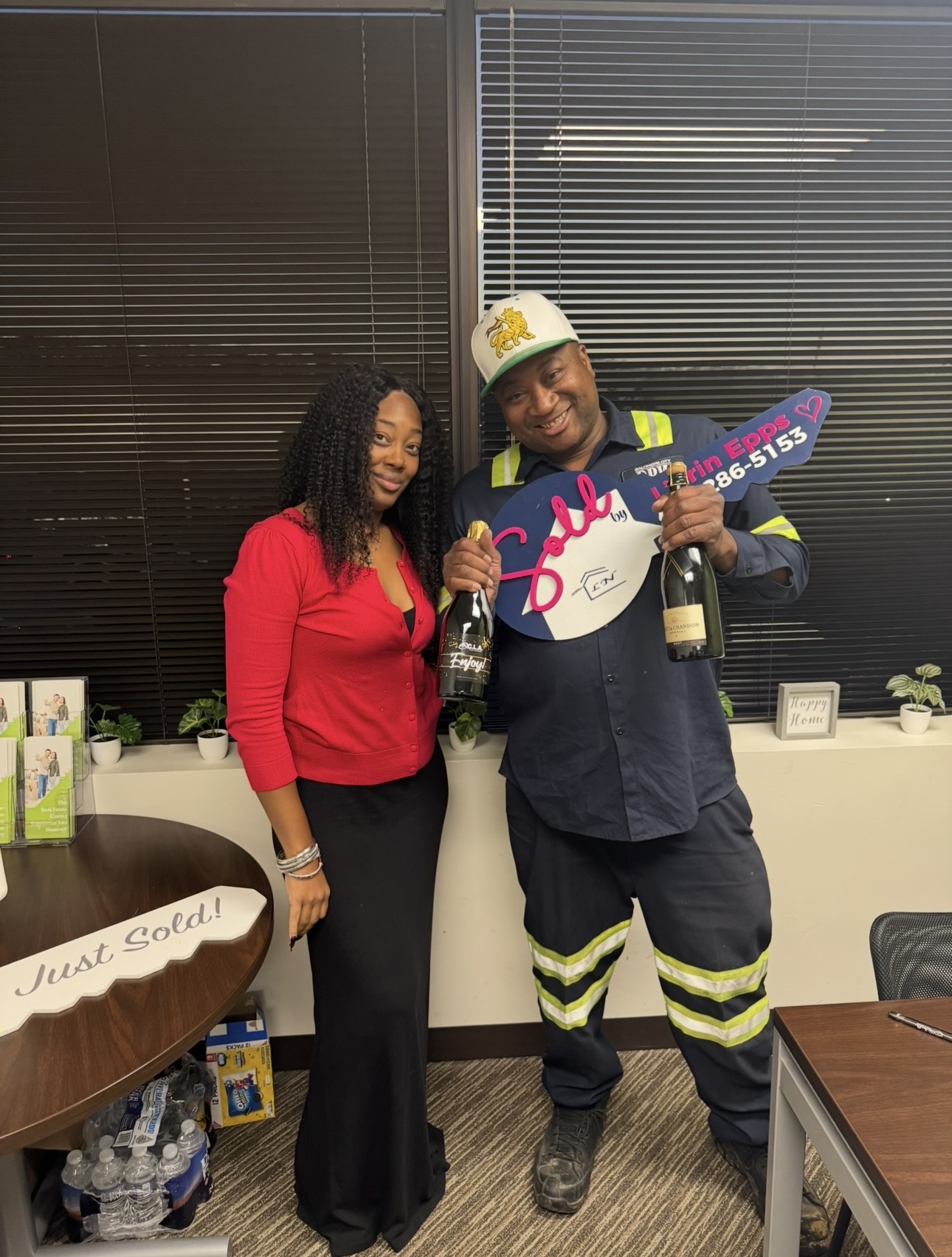 A woman and a man in a room, woman in red top and black pants, man in firefighter uniform holding a large key and a bottle.