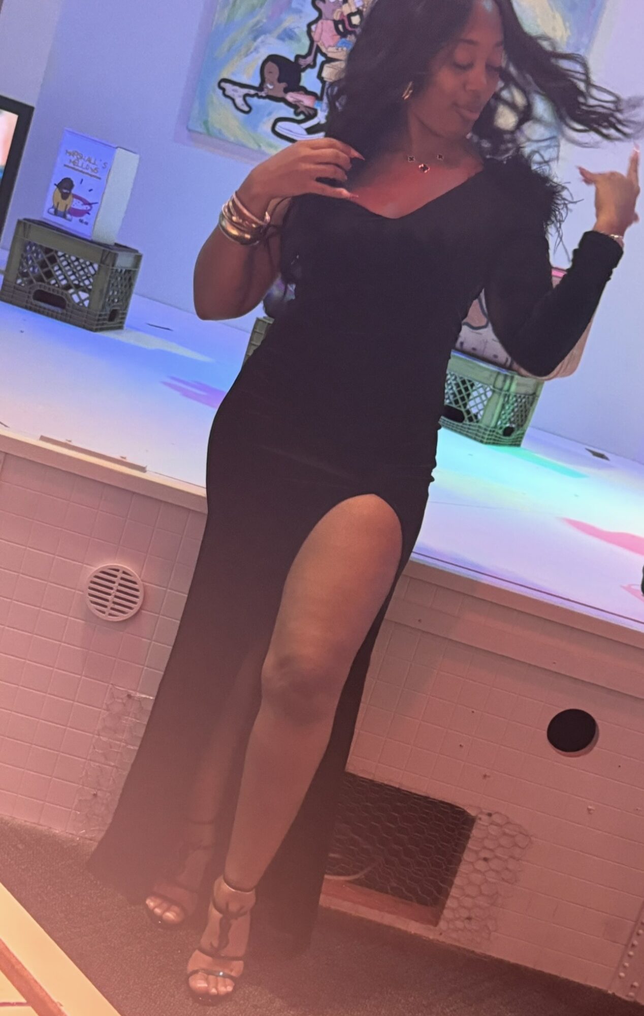Woman in a black dress with a high slit, dancing with hair flowing, in a colorful room.