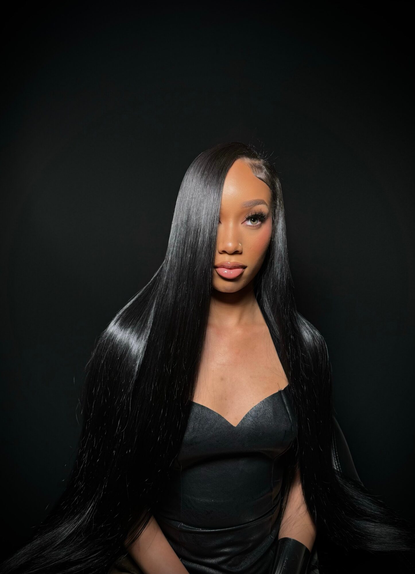 Woman with long, straight black hair wearing a black top, looking slightly to the side against a dark background.