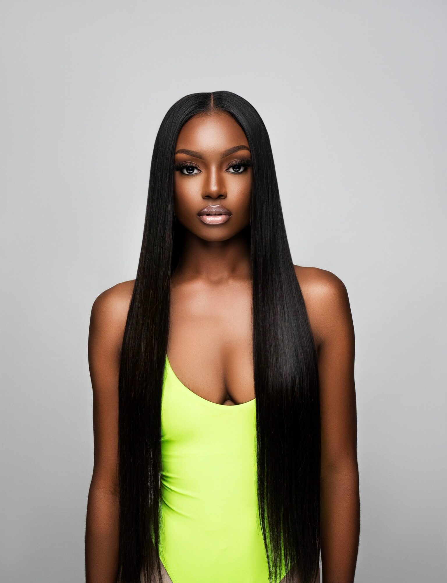 A woman with long, straight black hair and dark makeup, wearing a bright yellow top, facing forward against a plain background.