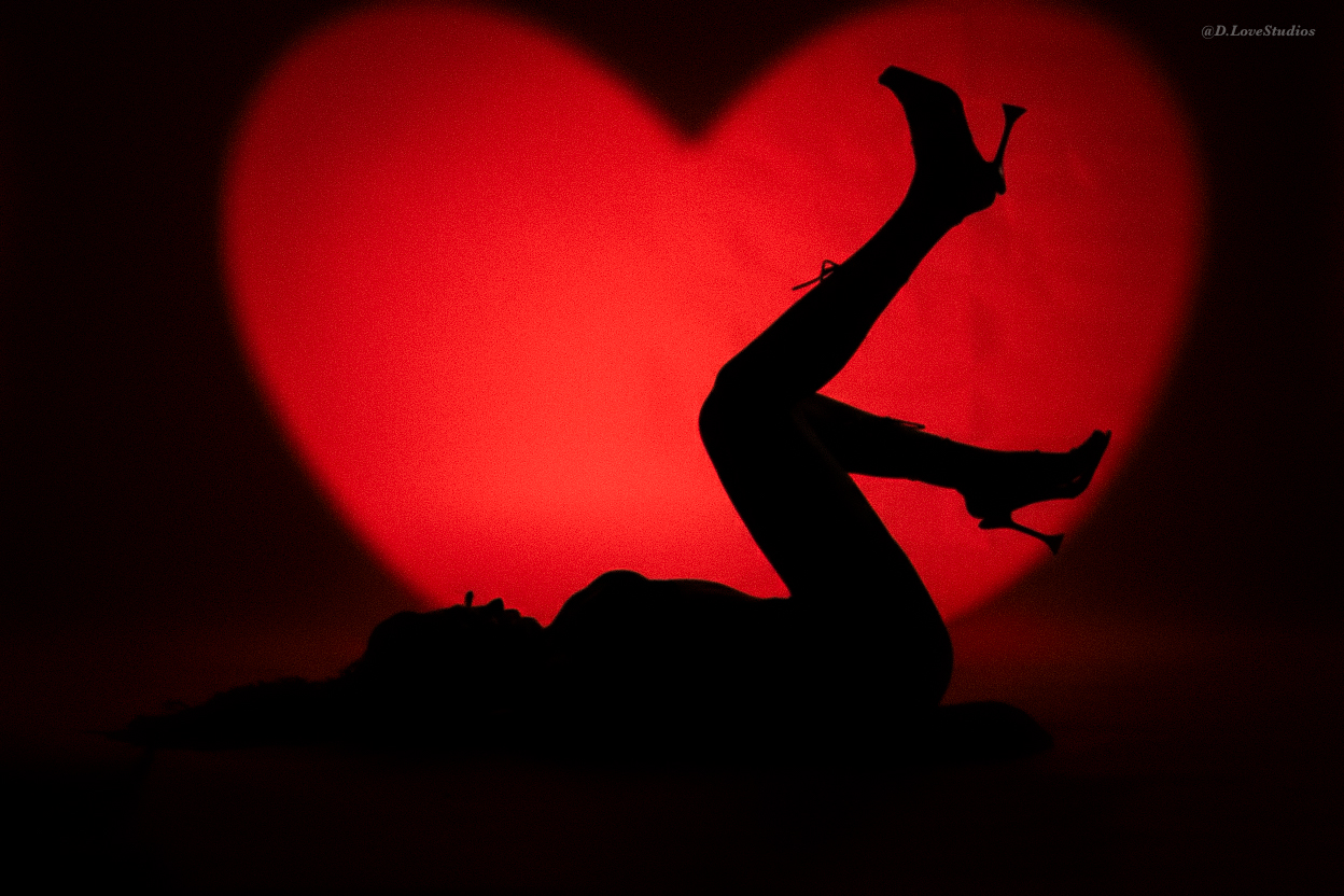 Silhouette of a person lying down with legs raised in front of a large red heart shape background.