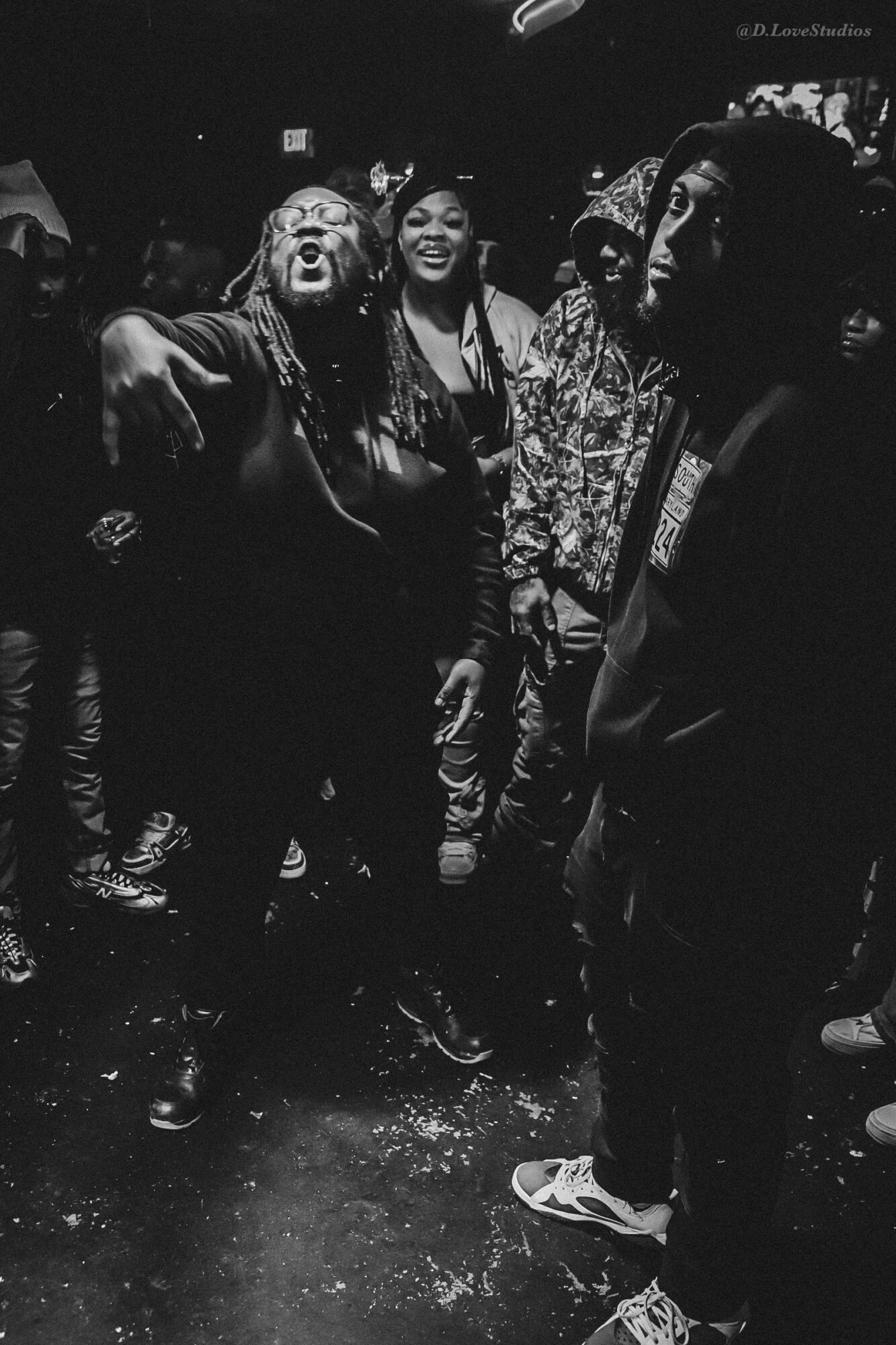 Group of people laughing and talking in a dark indoor setting, some with dreadlocks and casual clothing.