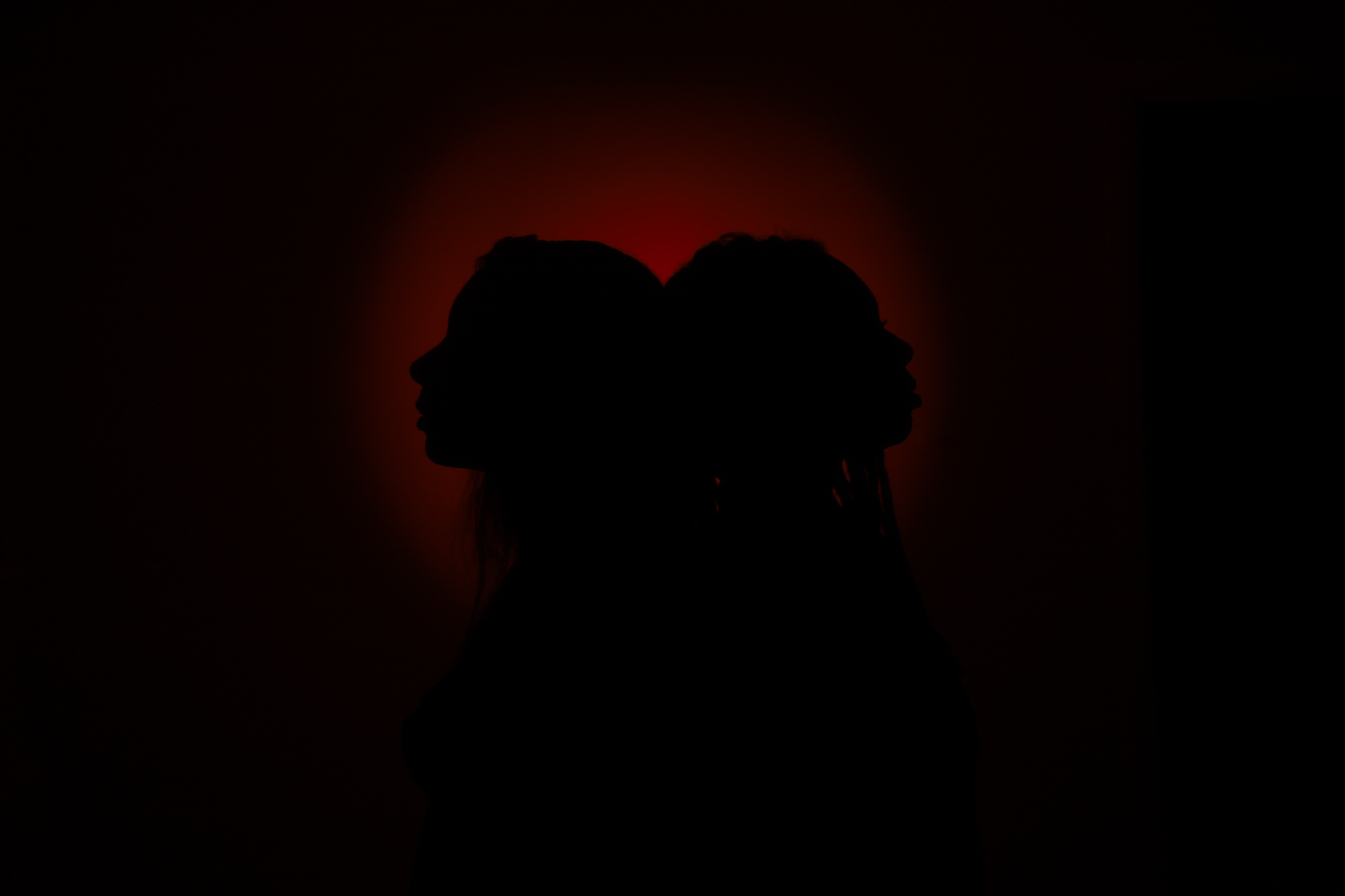 Two silhouetted people face opposite directions with a red glow behind them.