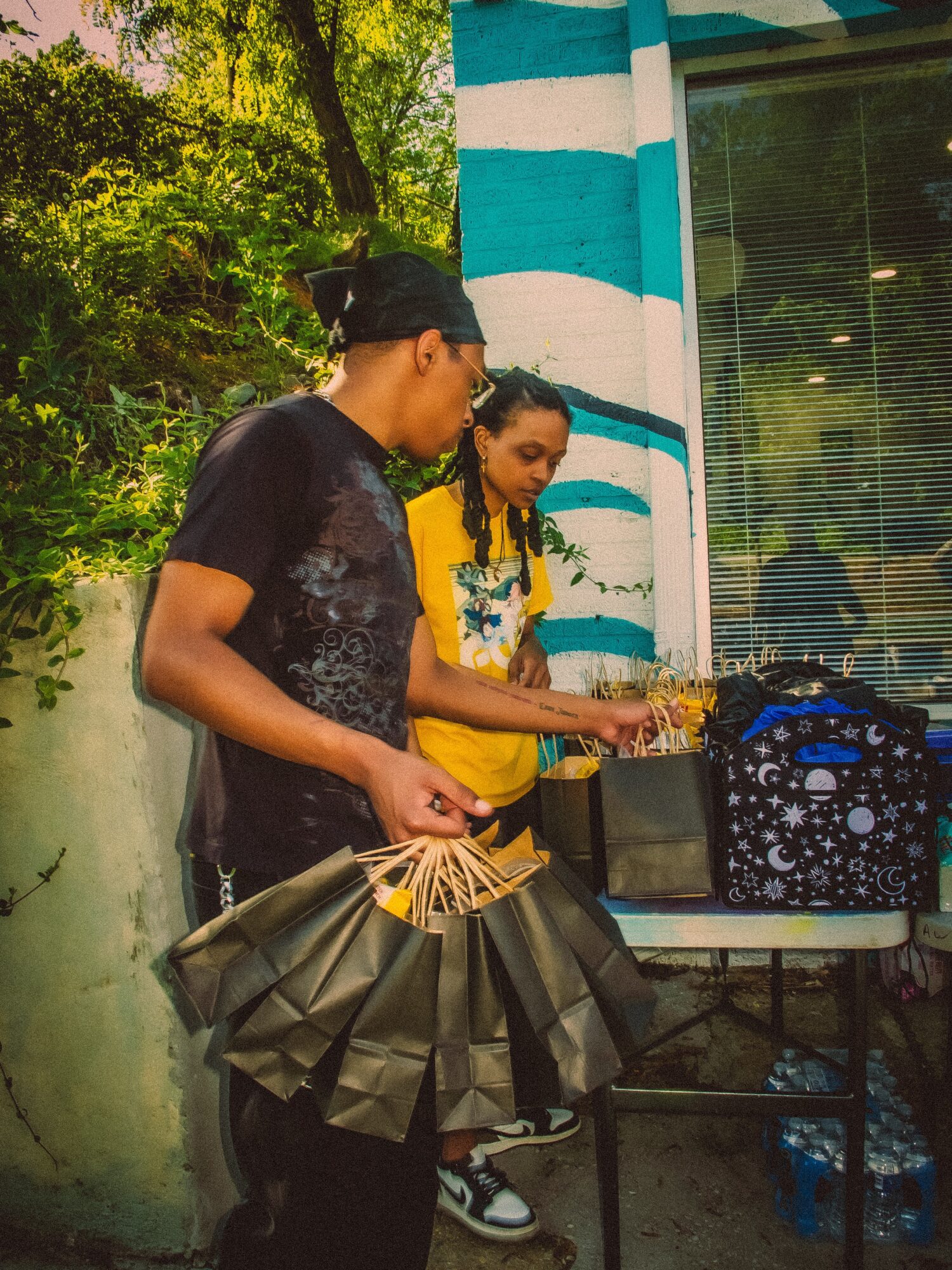 Two people standing outdoors near a striped blue and white building, with trees in the background, engaged in an activity.