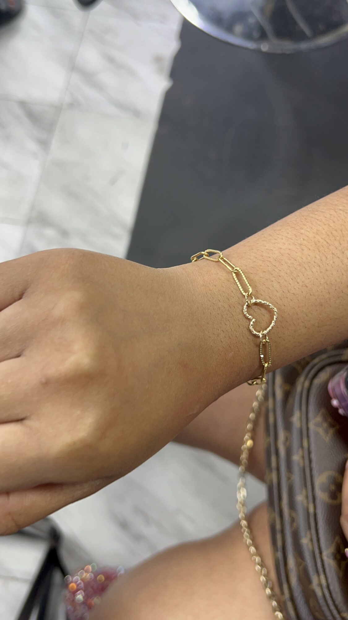 Close-up of a person's wrist wearing a gold bracelet with circular links, against a blurred background.
