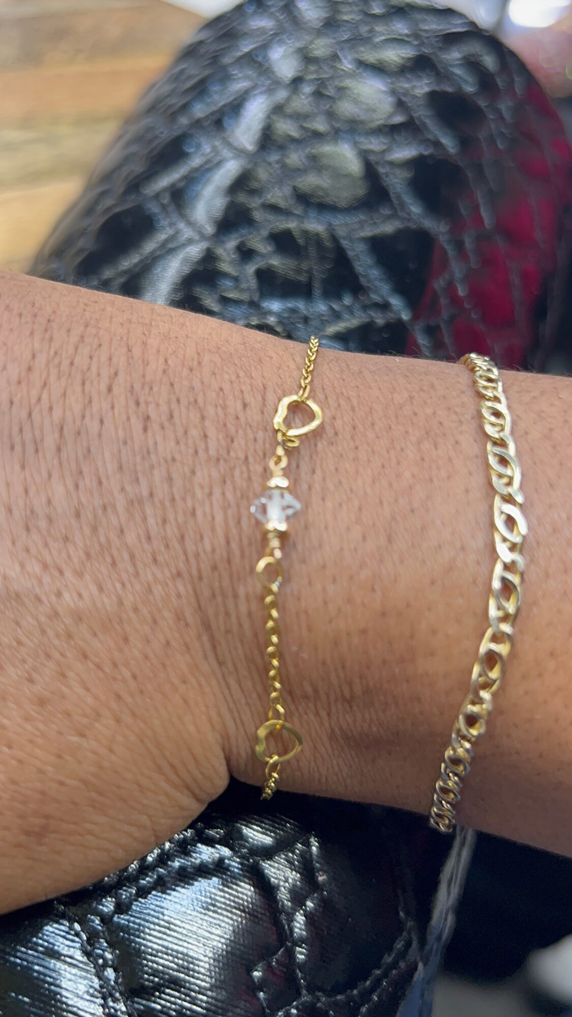 Close-up of a wrist with two gold bracelets, one with a small charm and a chain, and the other a thicker chain.