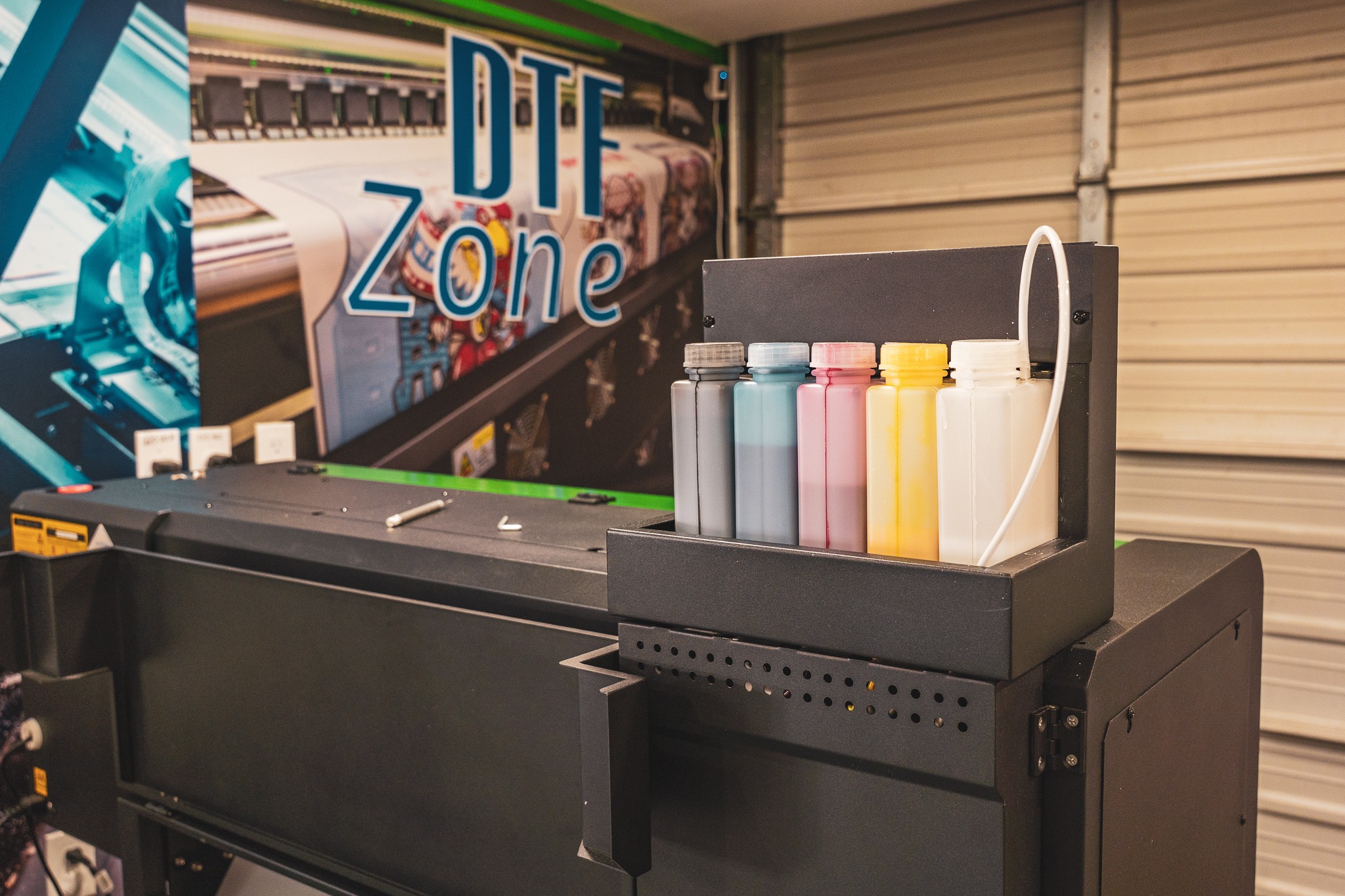 Printer with ink bottles and a sign reading 'DTF Zone' in a workshop setting.