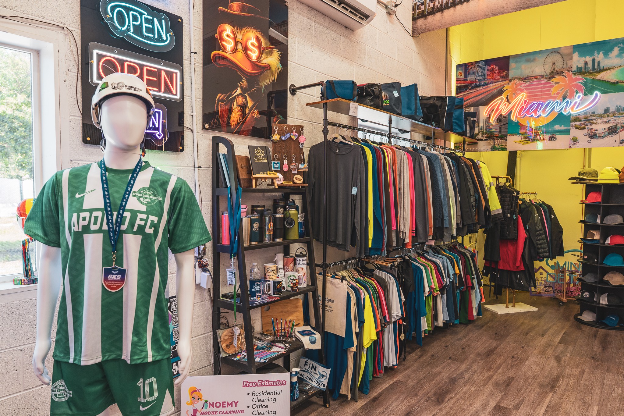 Clothing store interior with a mannequin in a green and white sports jersey, racks of clothes, and neon signs, wooden floor.
