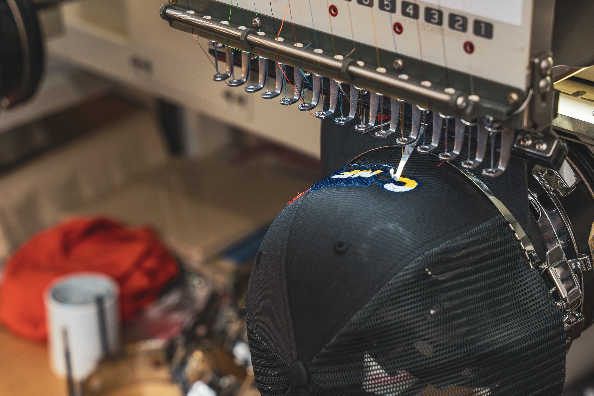 A machine embroidering a black fabric with a design, with spools and tools in the background.