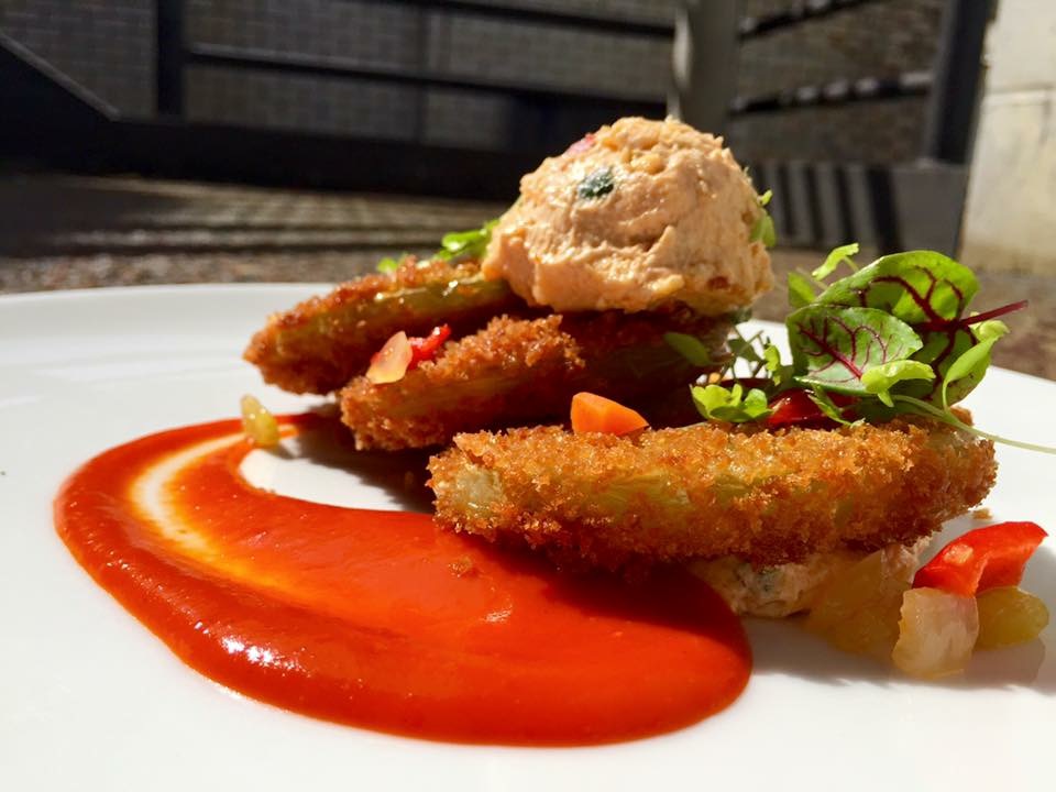 Fried fish fillets with sauce, garnished with microgreens and a scoop of potato salad on a white plate.