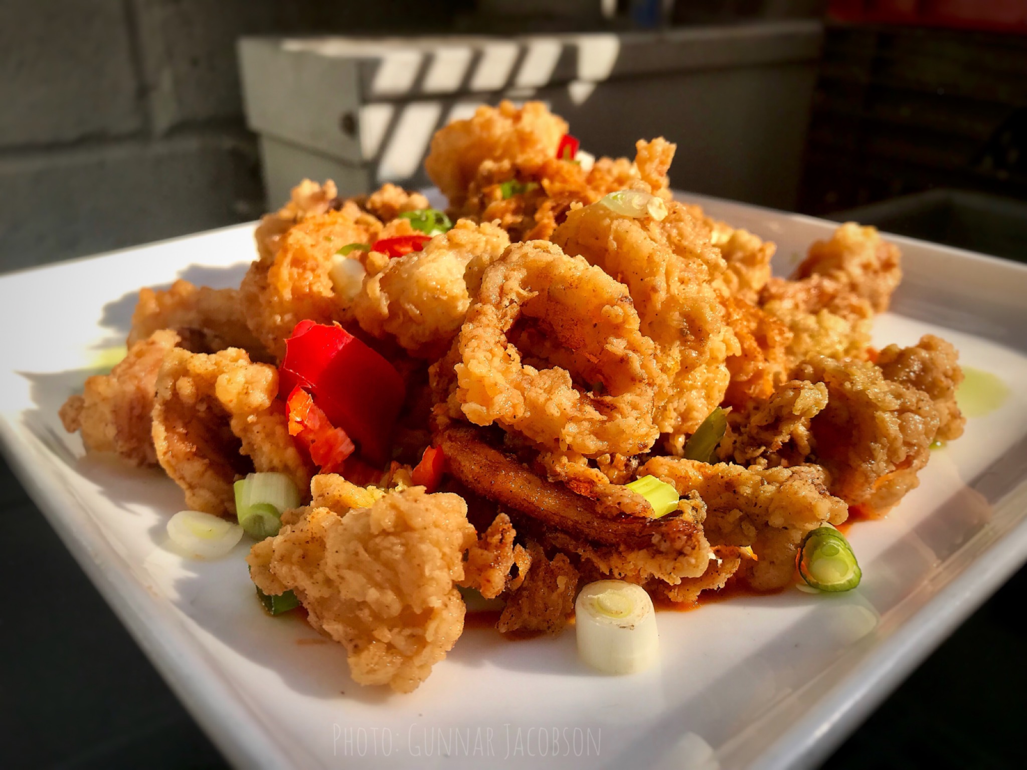 Fried calamari with chopped red and green peppers on a white plate.