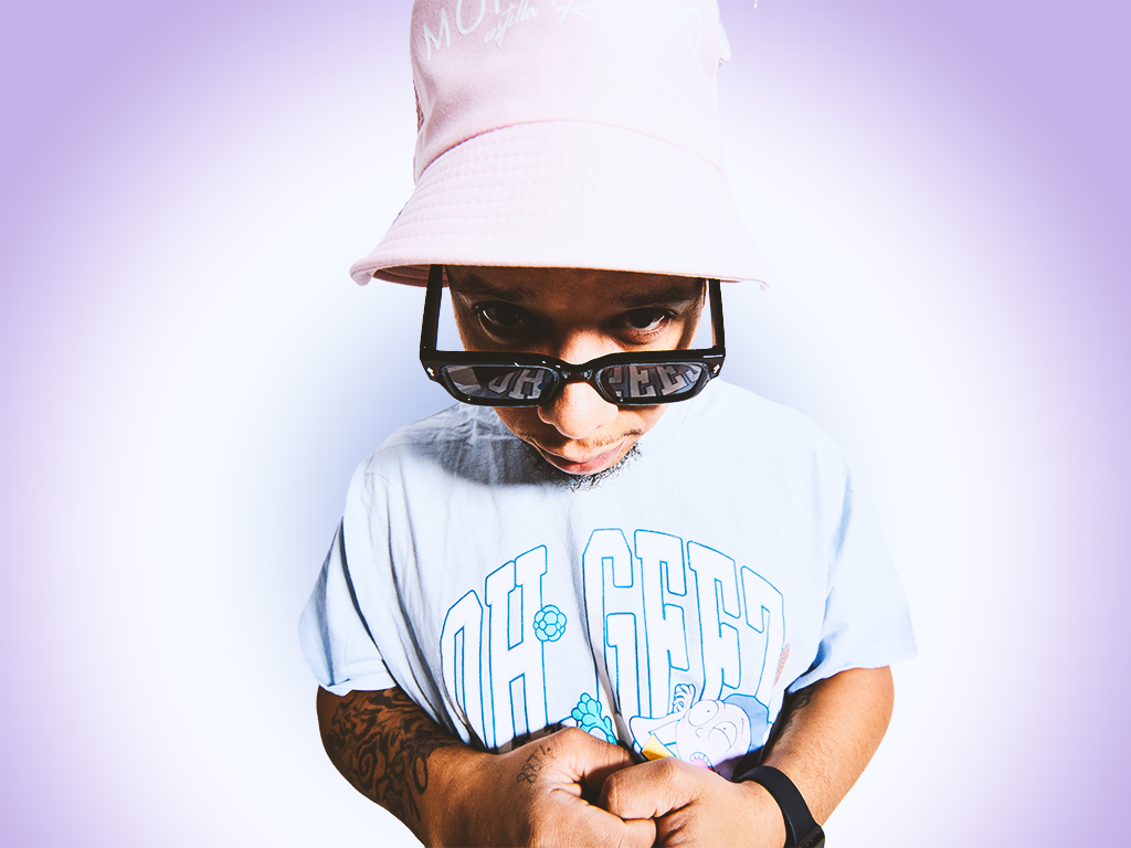 Child wearing a pink hat, sunglasses, and a light blue shirt, looking down with crossed arms, against a purple background.