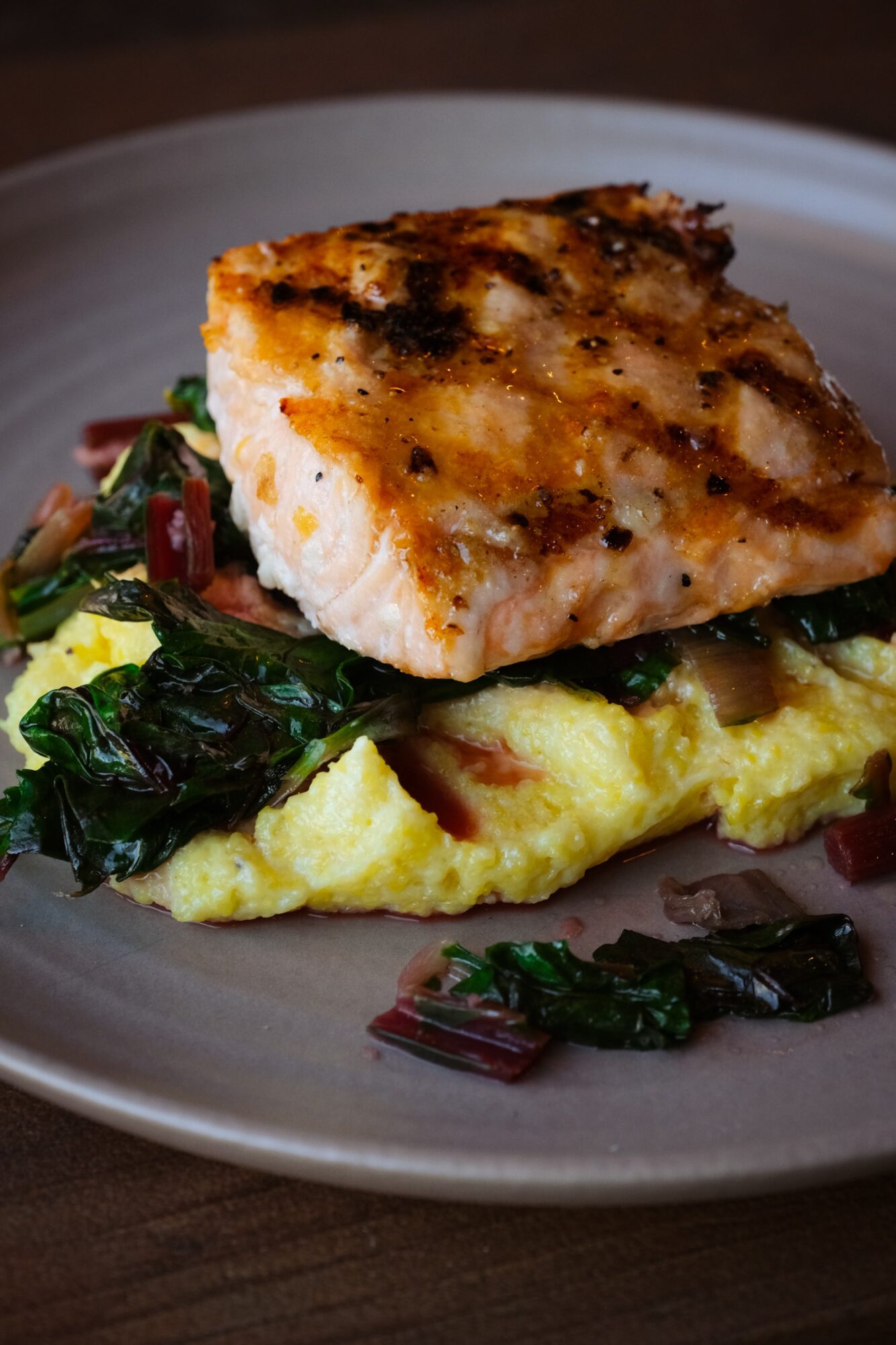 Baked fish fillet on scrambled eggs with sautéed greens on a plate.