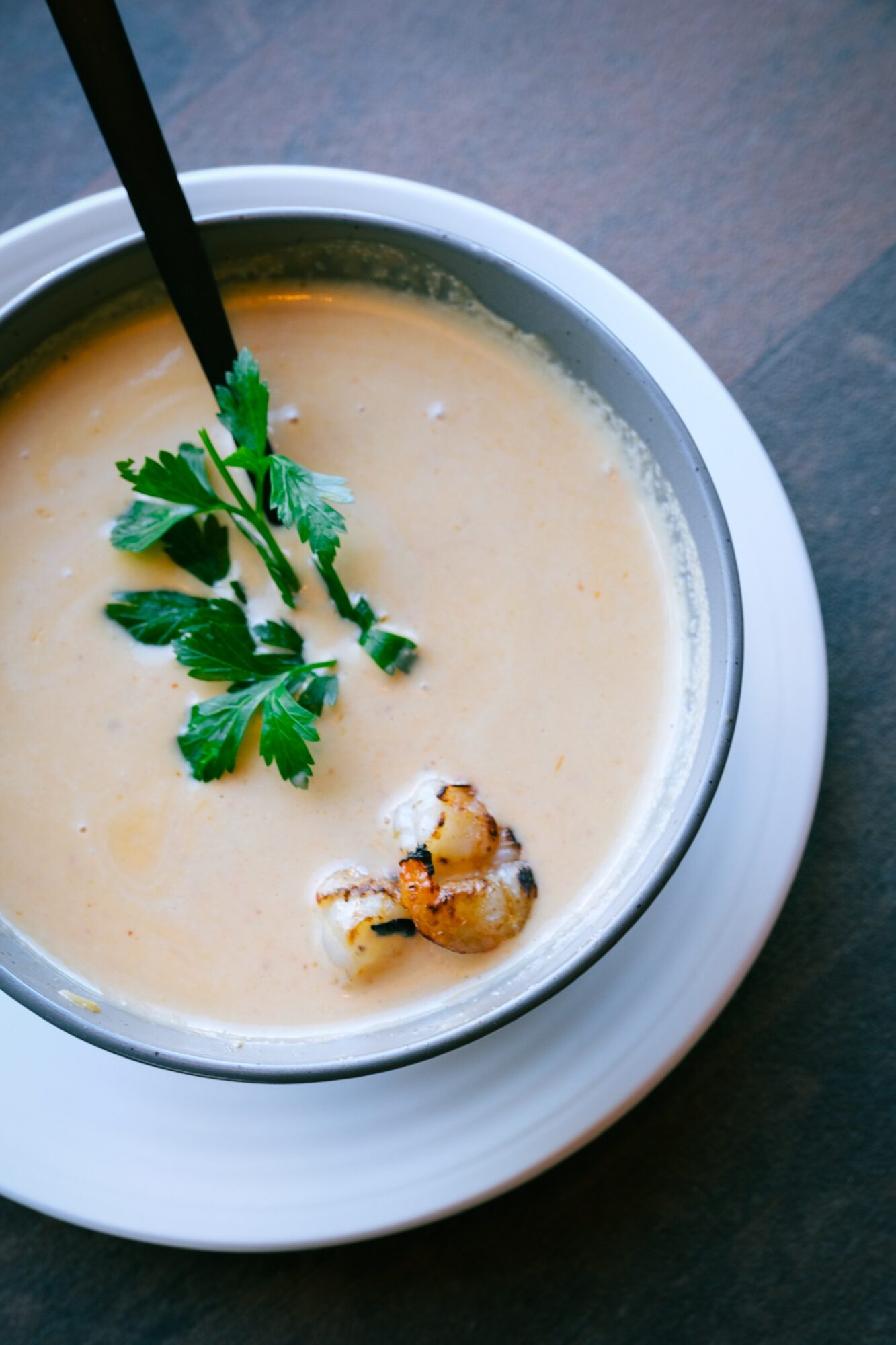Creamy soup in a white bowl garnished with parsley and a small piece of bread, on a dark wooden surface.