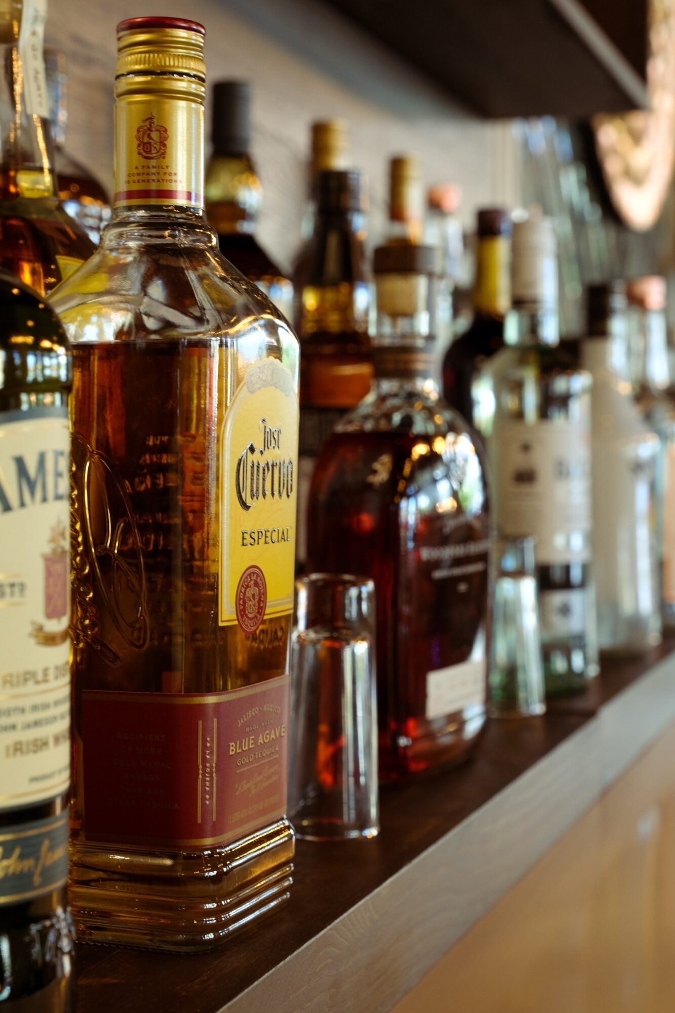 Various liquor bottles on a shelf, with a focus on a tequila bottle in the foreground, background slightly blurred.
