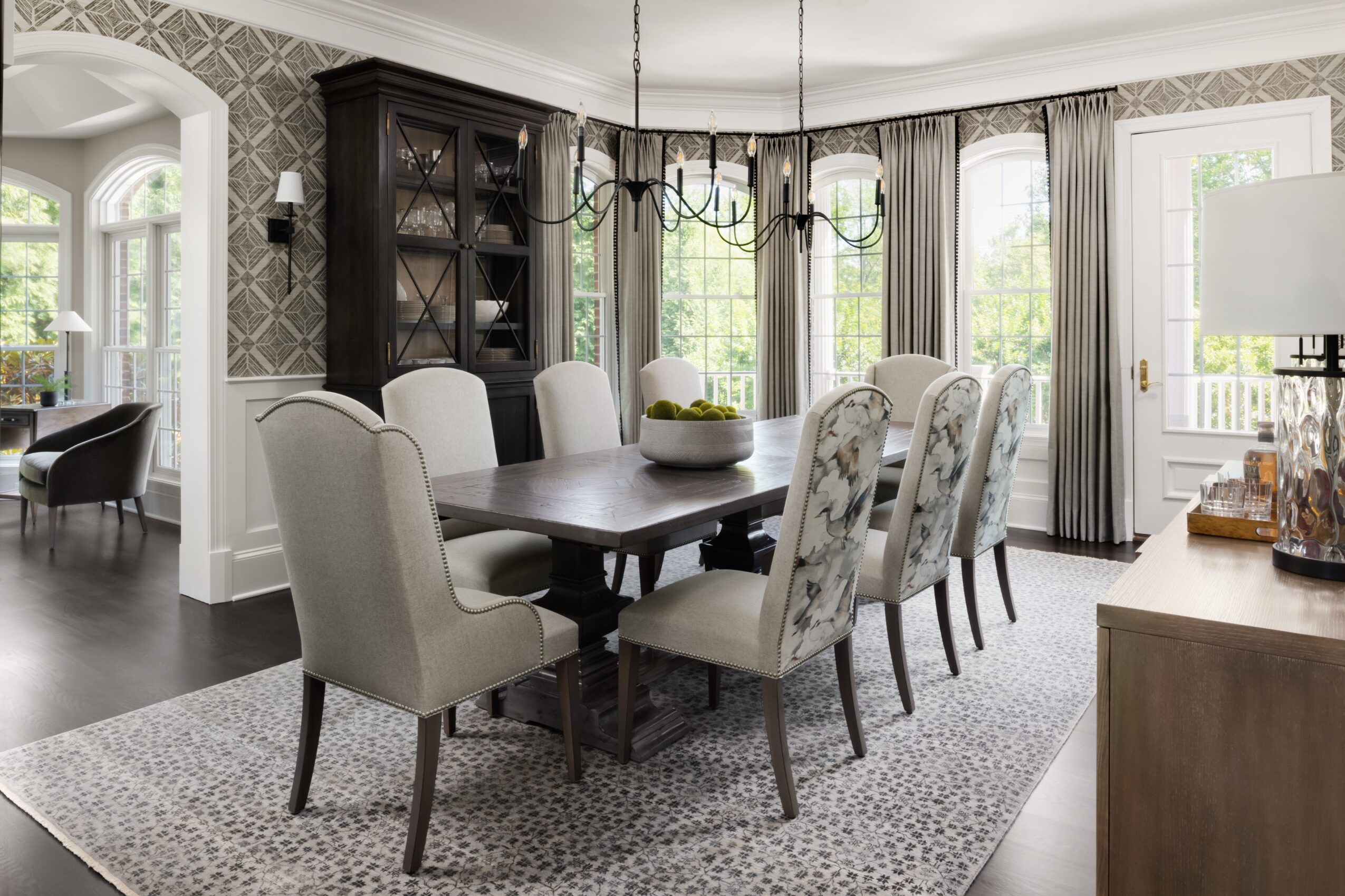 Dining room with a dark wood cabinet, large window, and a table with eight upholstered chairs, rug, and chandelier.