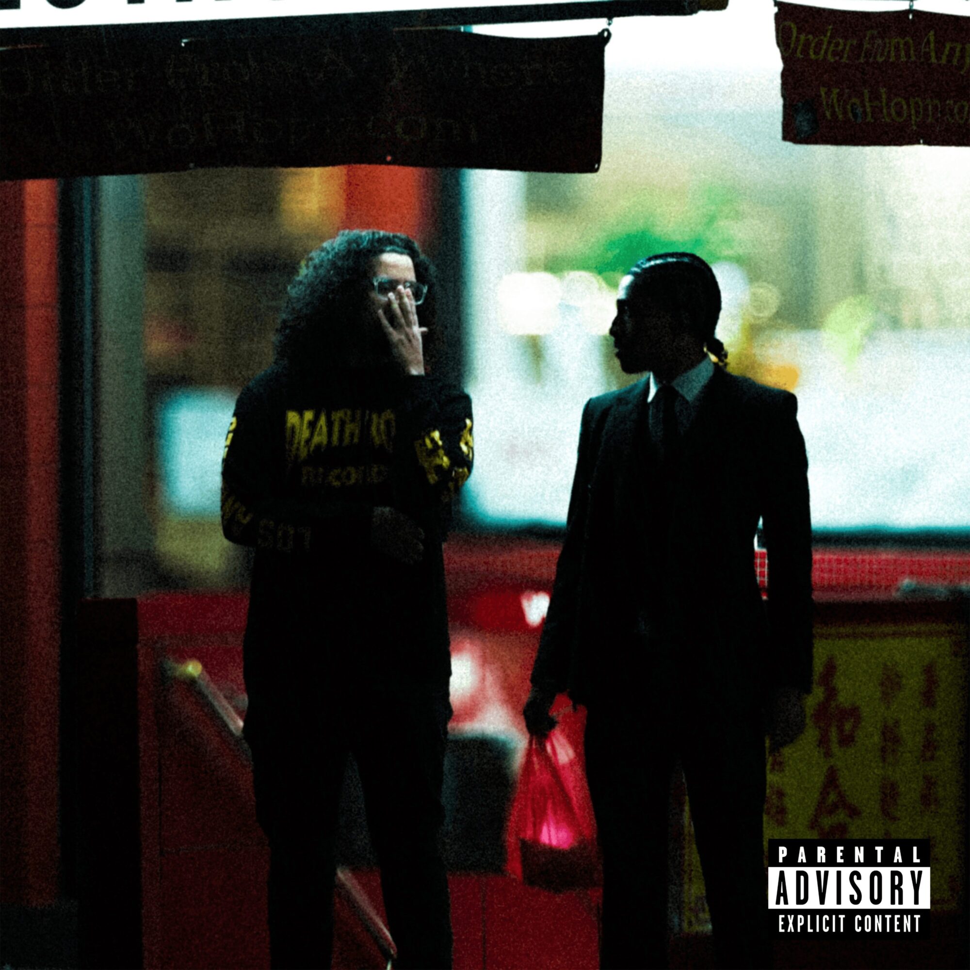 Two people in silhouette, one with curly hair and glasses, the other in a suit holding a bag, standing outside.
