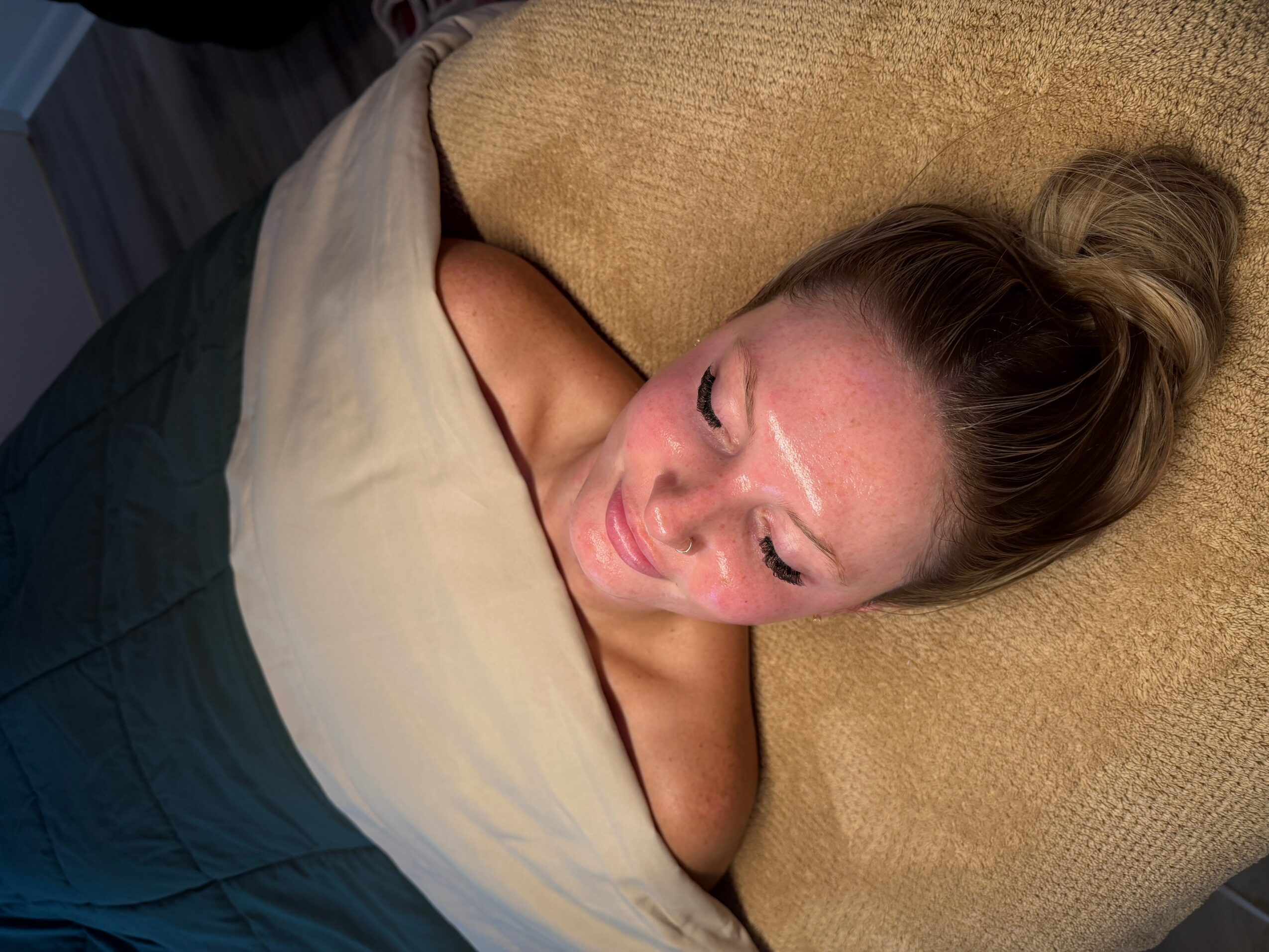 Woman lying on a couch with her head on a cushion, wrapped in a blanket, eyes closed, relaxed.