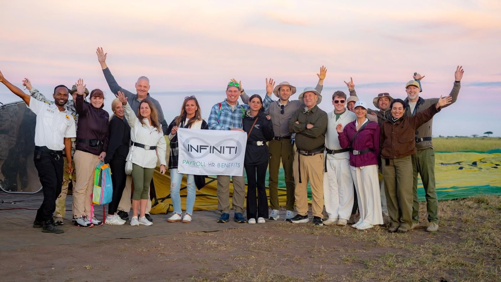 Group of people outdoors holding a banner, waving, with a landscape background, sky, and fields.