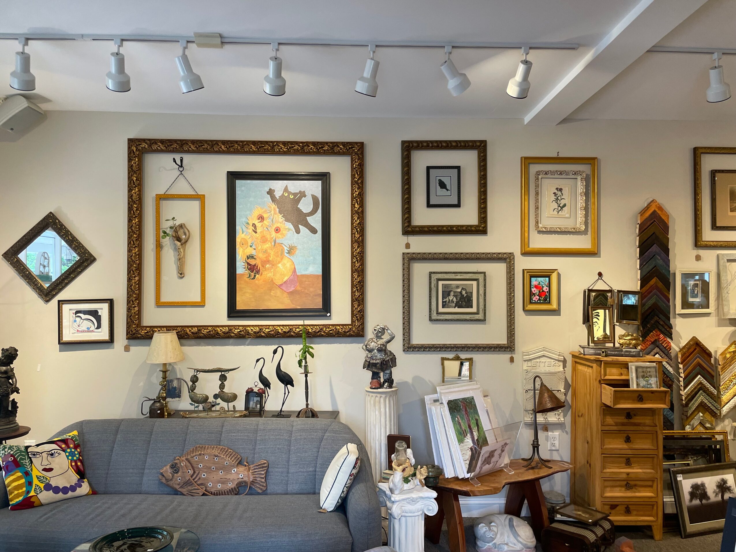 Interior of a room with framed artwork and decorative items on the wall, a gray sofa, and wooden furniture.