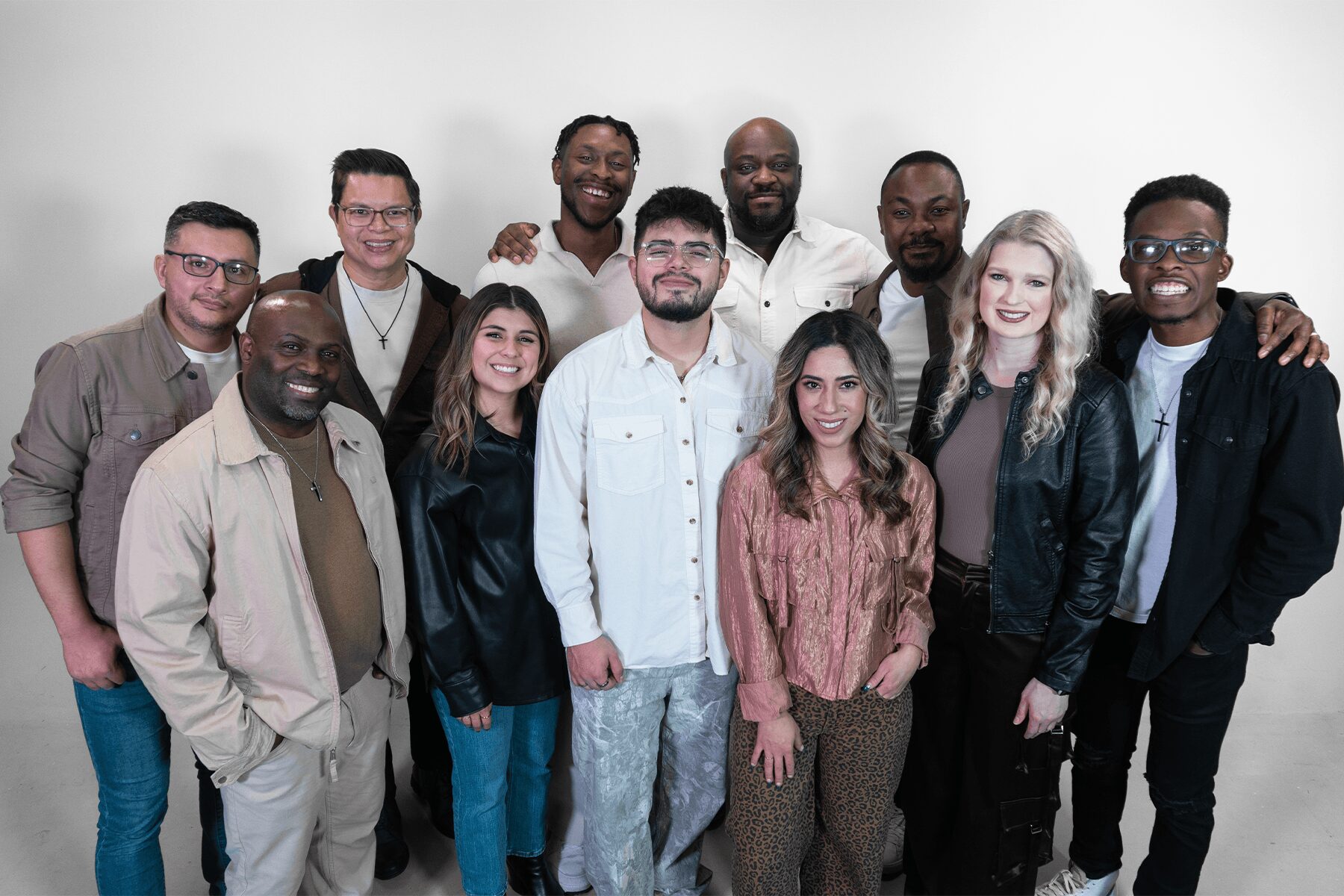 Group of twelve diverse people standing together, smiling, against a plain white background.
