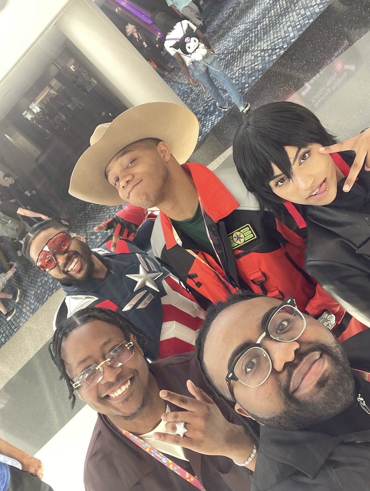 Group of five people smiling and posing for a photo indoors, some wearing costumes and accessories.