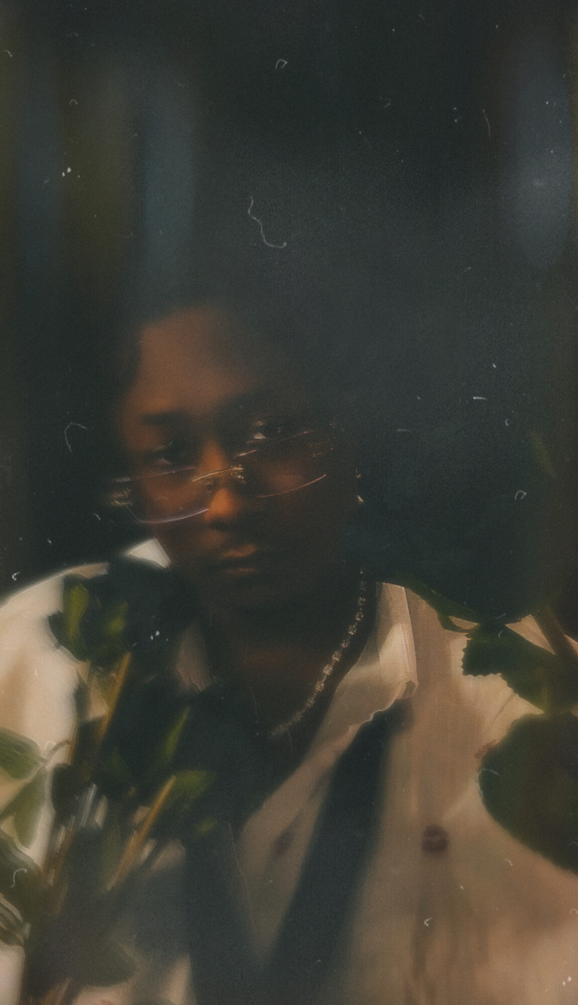 Person with glasses and dark hair, wearing a patterned shirt, in a dimly lit environment.