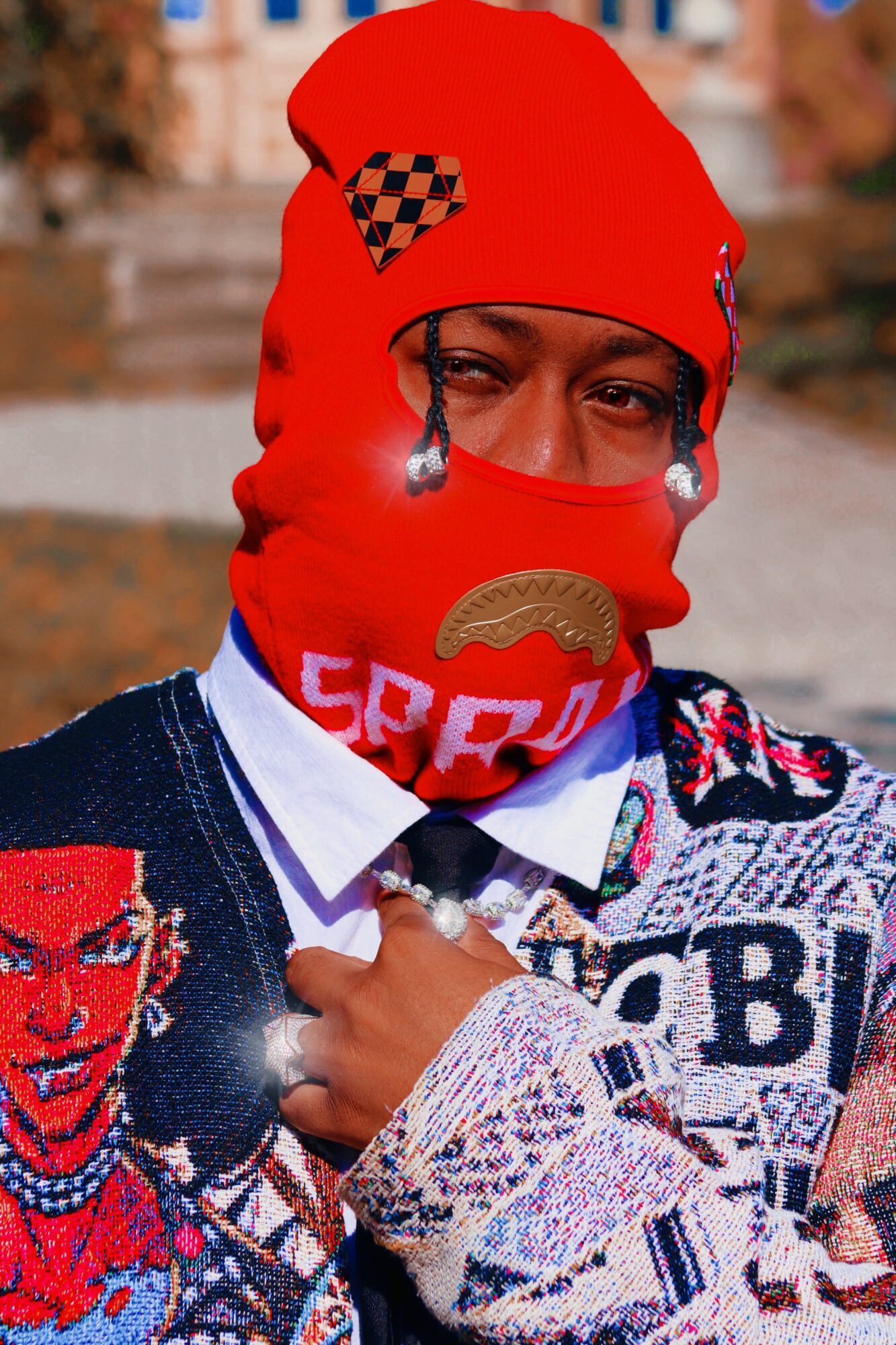 Person wearing a red hat and face covering with various patterns, including a checkered patch, outdoors with blurred background.