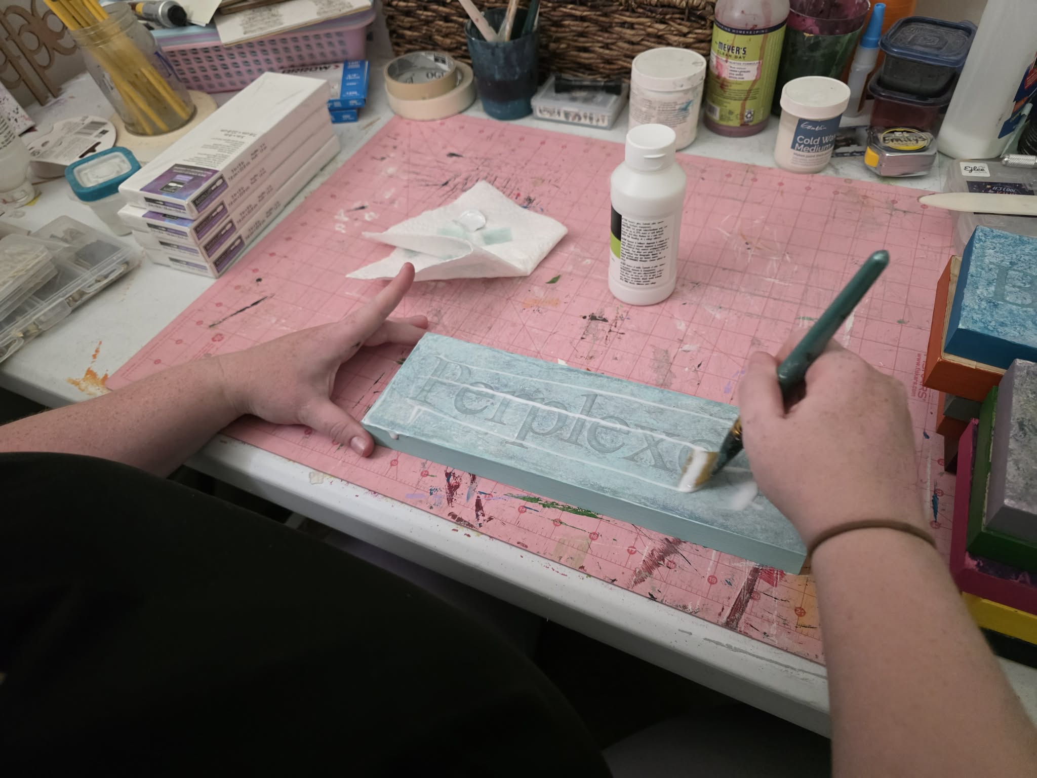Person working on a craft project with a blue foam board, markers, and supplies on a pink cutting mat.