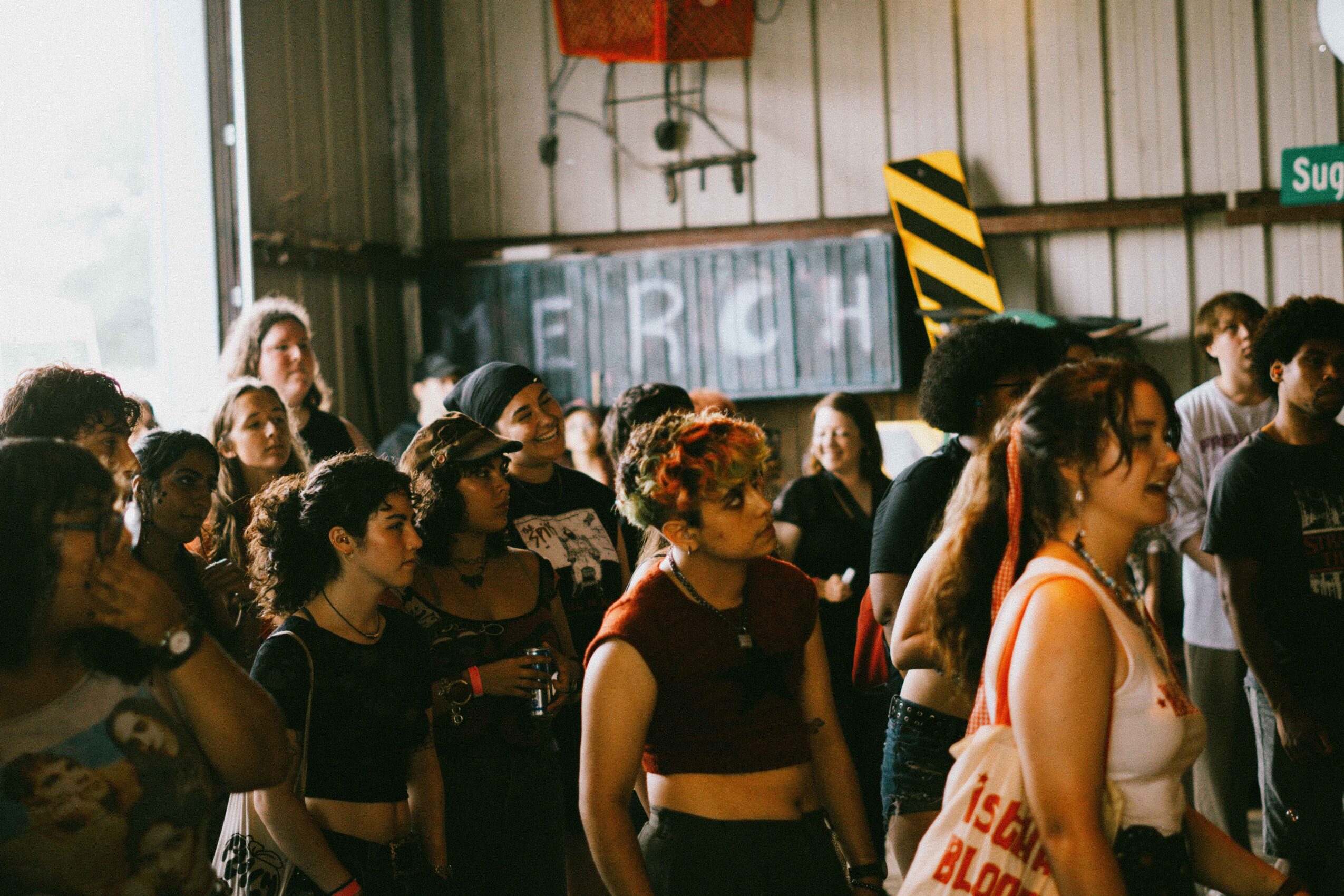 Group of people gathered indoors, some with colorful hair, in front of a wall with graffiti and a yellow and black striped sign.