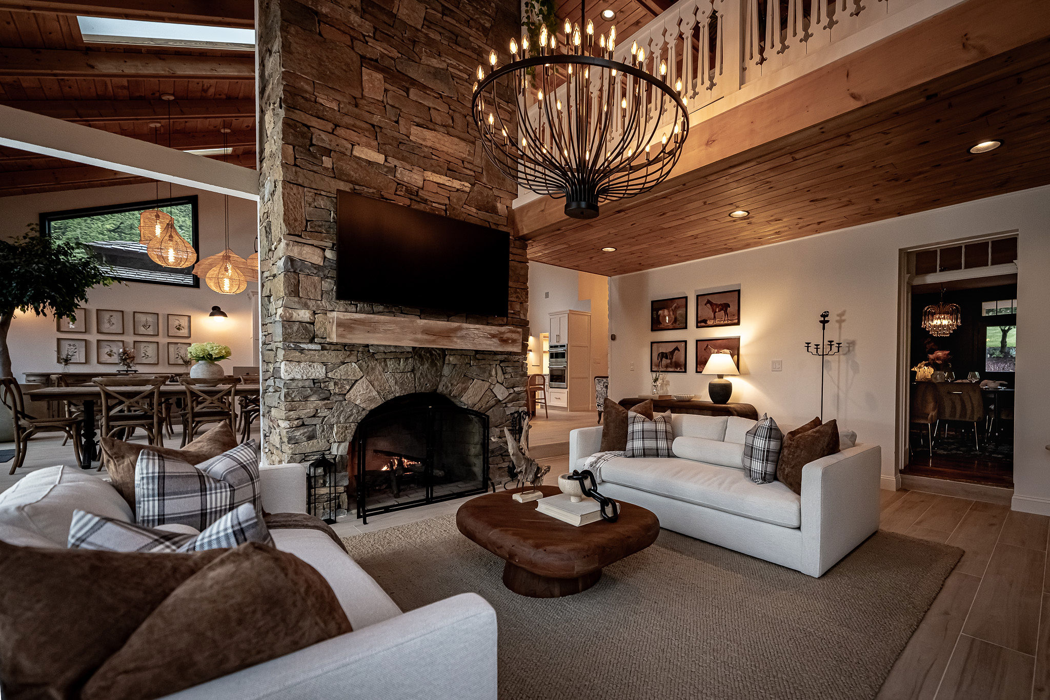 Living room with stone fireplace, wooden ceiling, chandelier, white sofas, and a wooden coffee table.