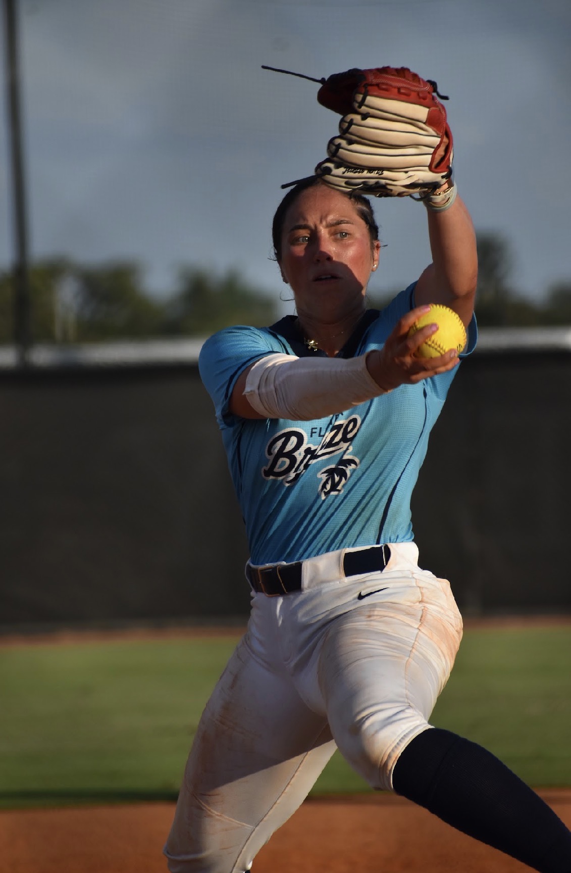 Baseball player in a blue uniform throws a cake with a baseball glove, outdoors on a field.