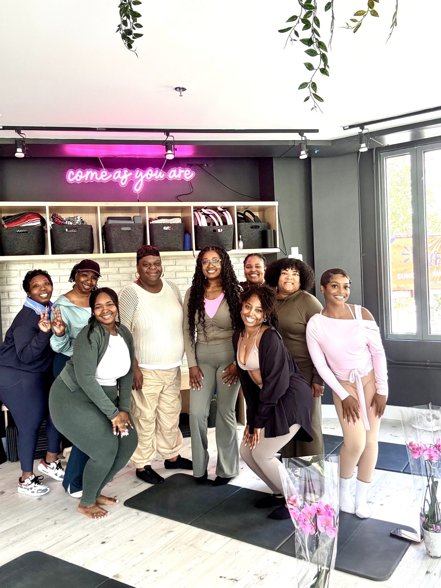 Group of nine people standing inside a store with a neon sign and shelves behind them.