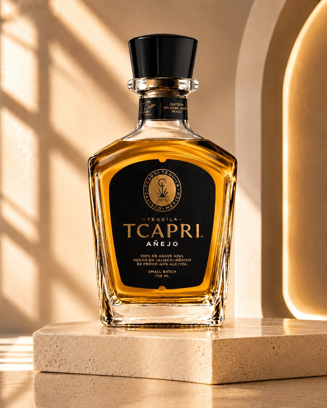 Bottle of Tcapri Añejo liquor on a beige surface with warm lighting and shadows, background with window and arch.