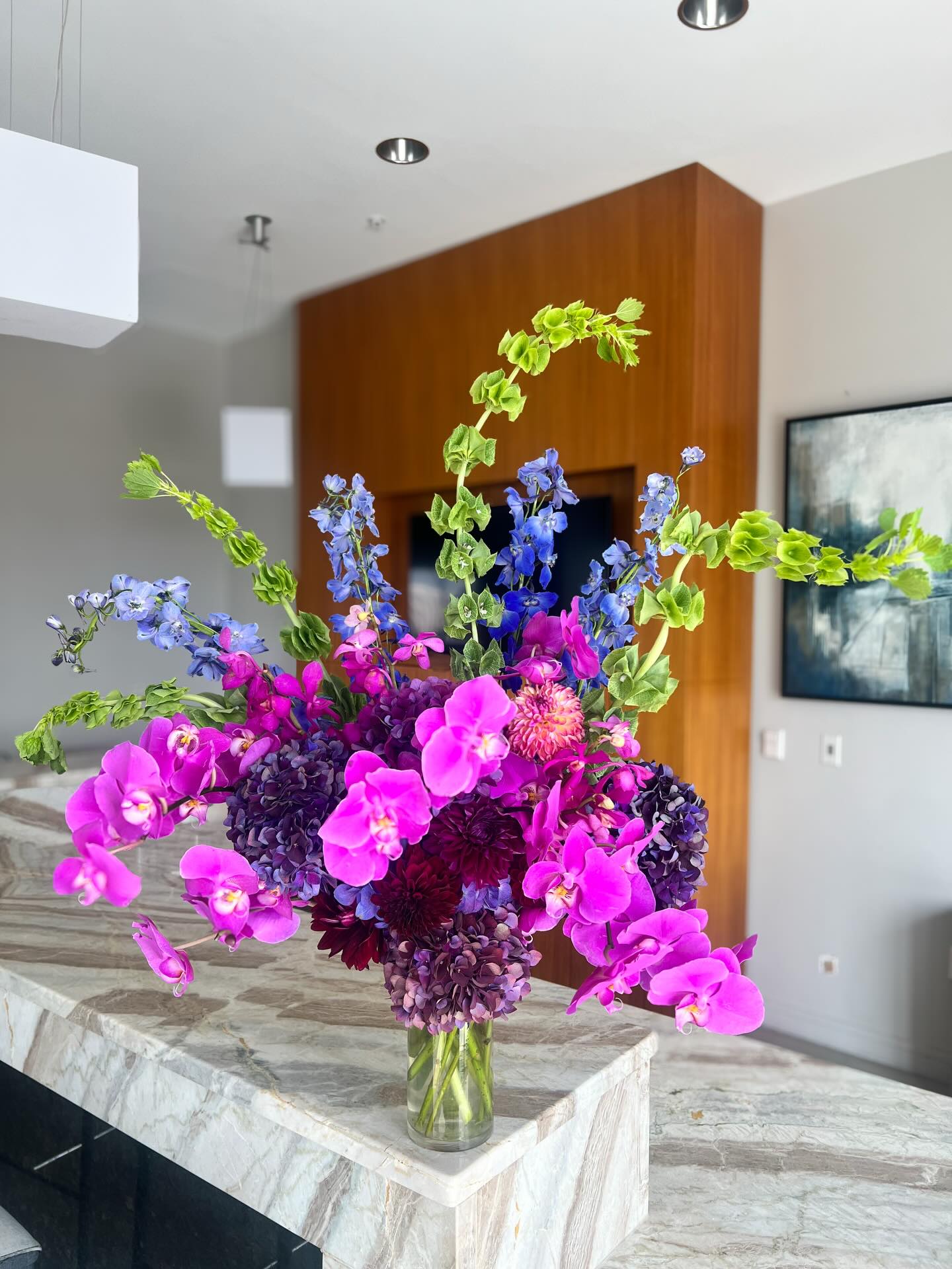 Vase with pink, purple, and blue flowers on a marble table in a modern room.