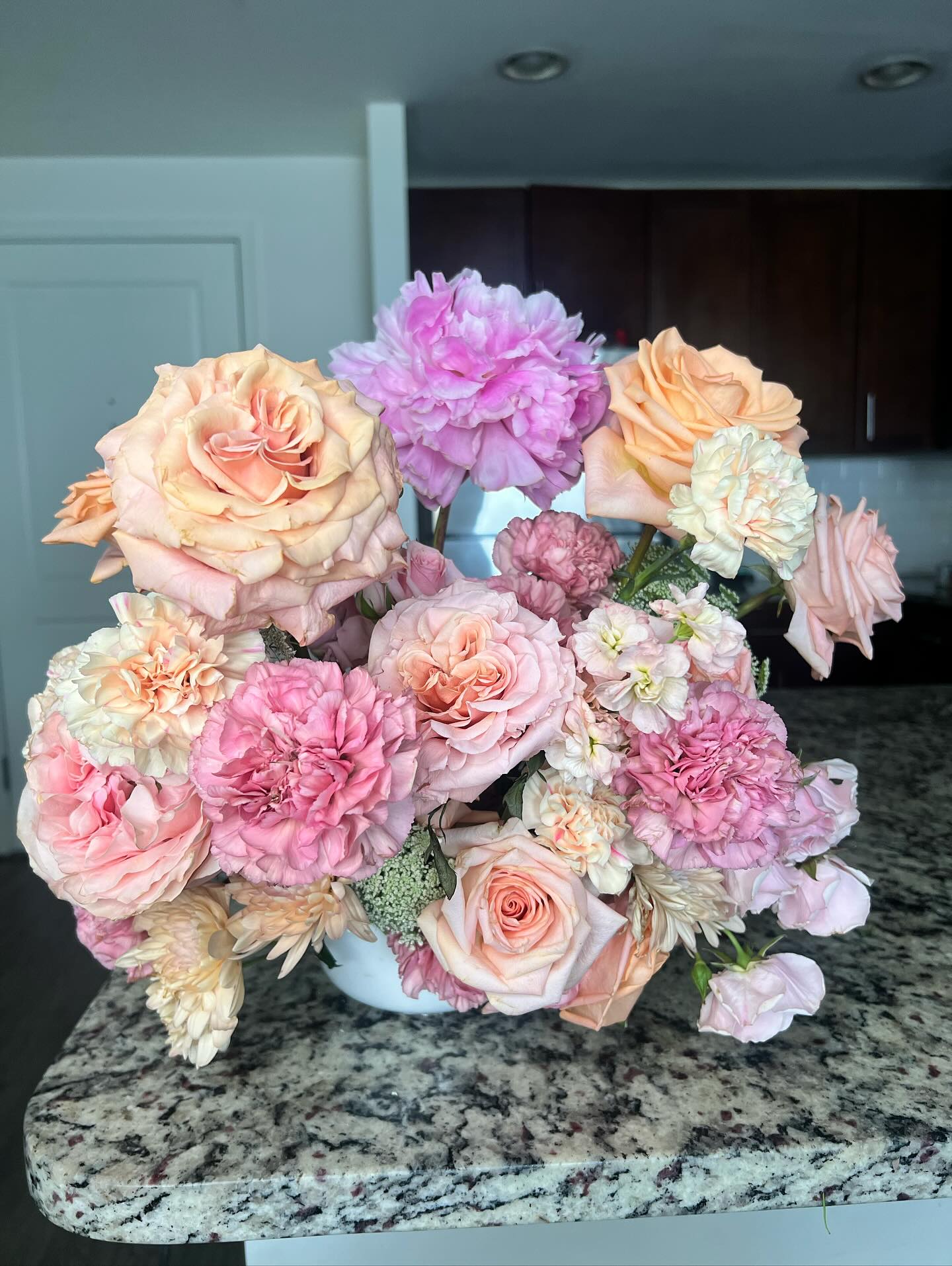 Arrangement of pink, peach, and white flowers on a granite countertop in a kitchen.