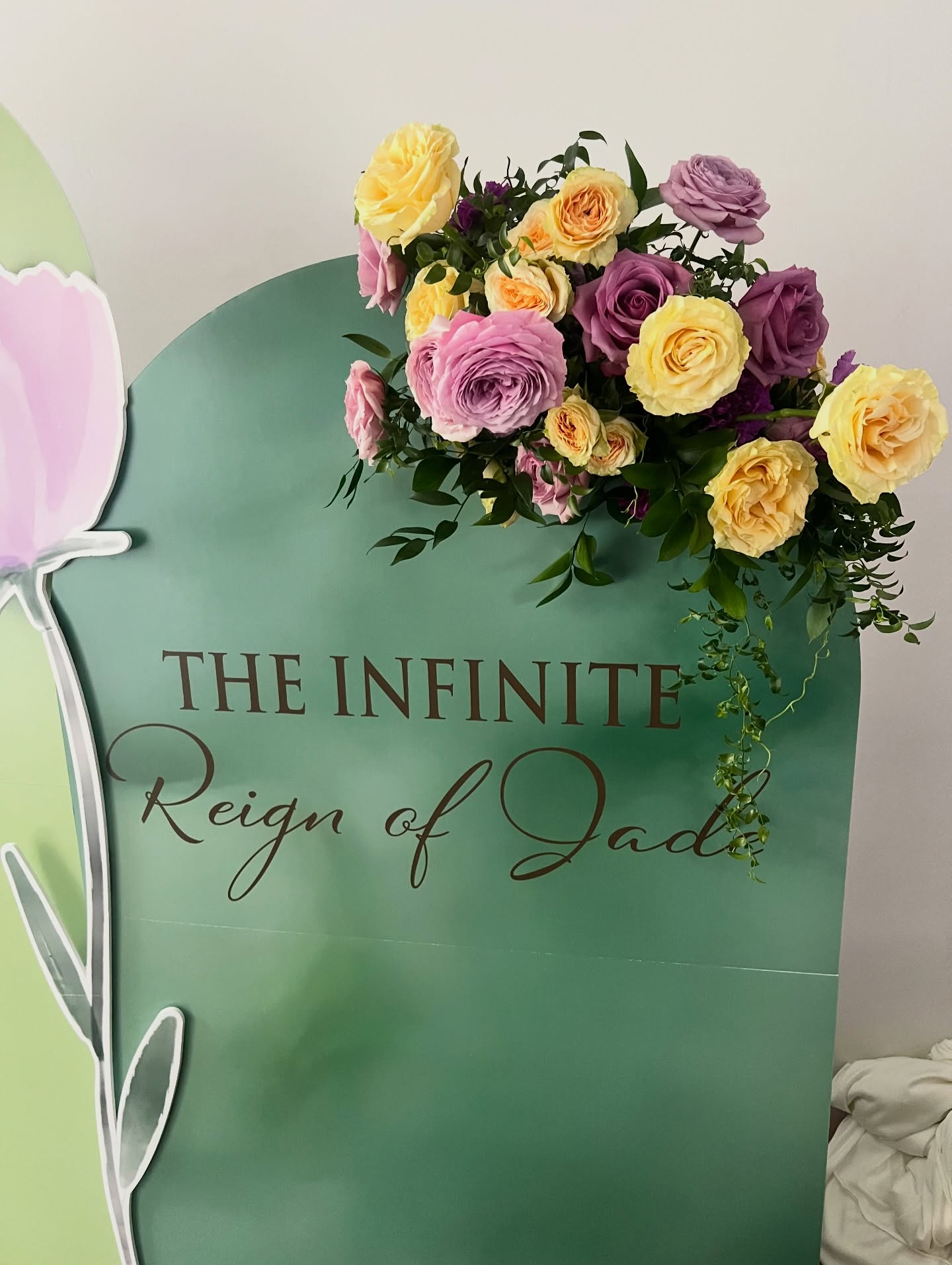 Flower arrangement with yellow, purple, and pink flowers in a green vase, with text reading 'The Infinite Reign of Jade'.