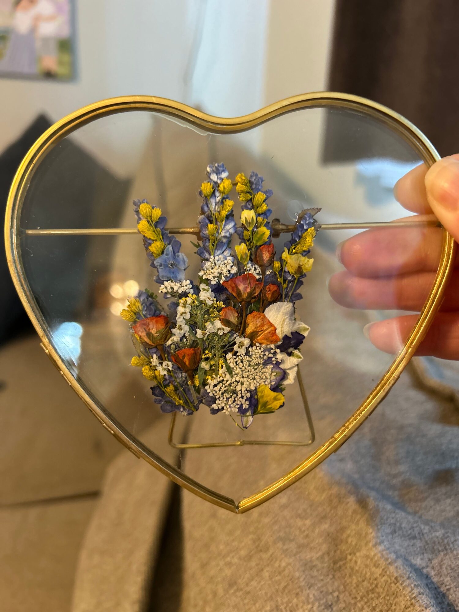 Person holding a heart-shaped mirror with a bouquet of colorful dried flowers reflected inside.